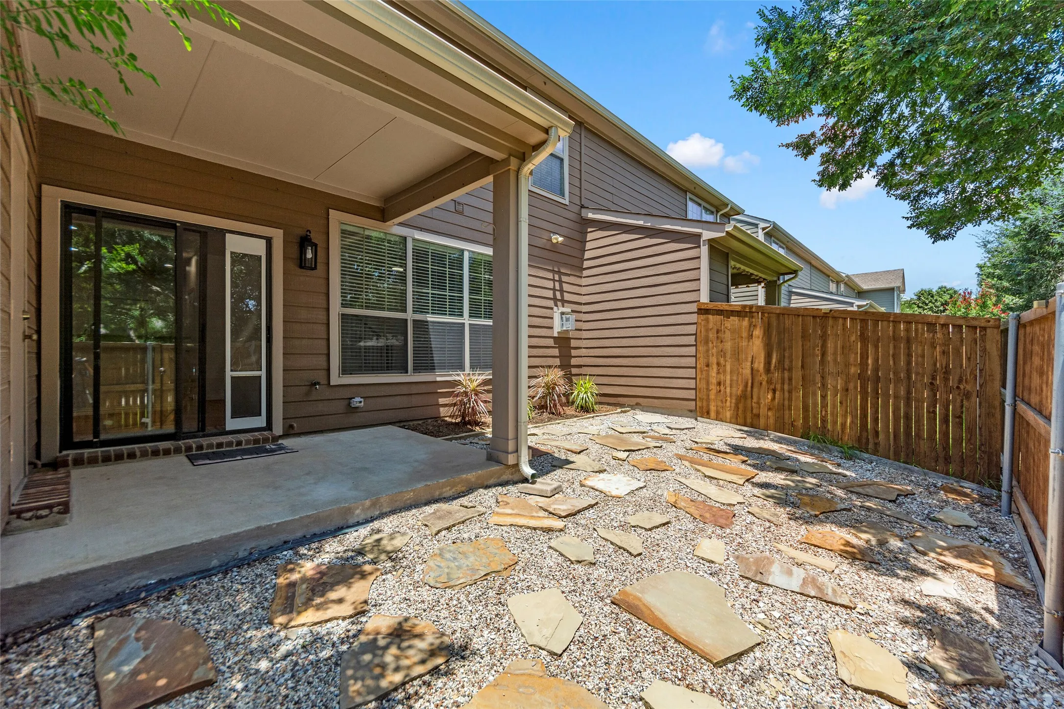 Private outdoor area featuring a concrete patio, gravel landscaping with irregular stone pavers, and a wood privacy fence