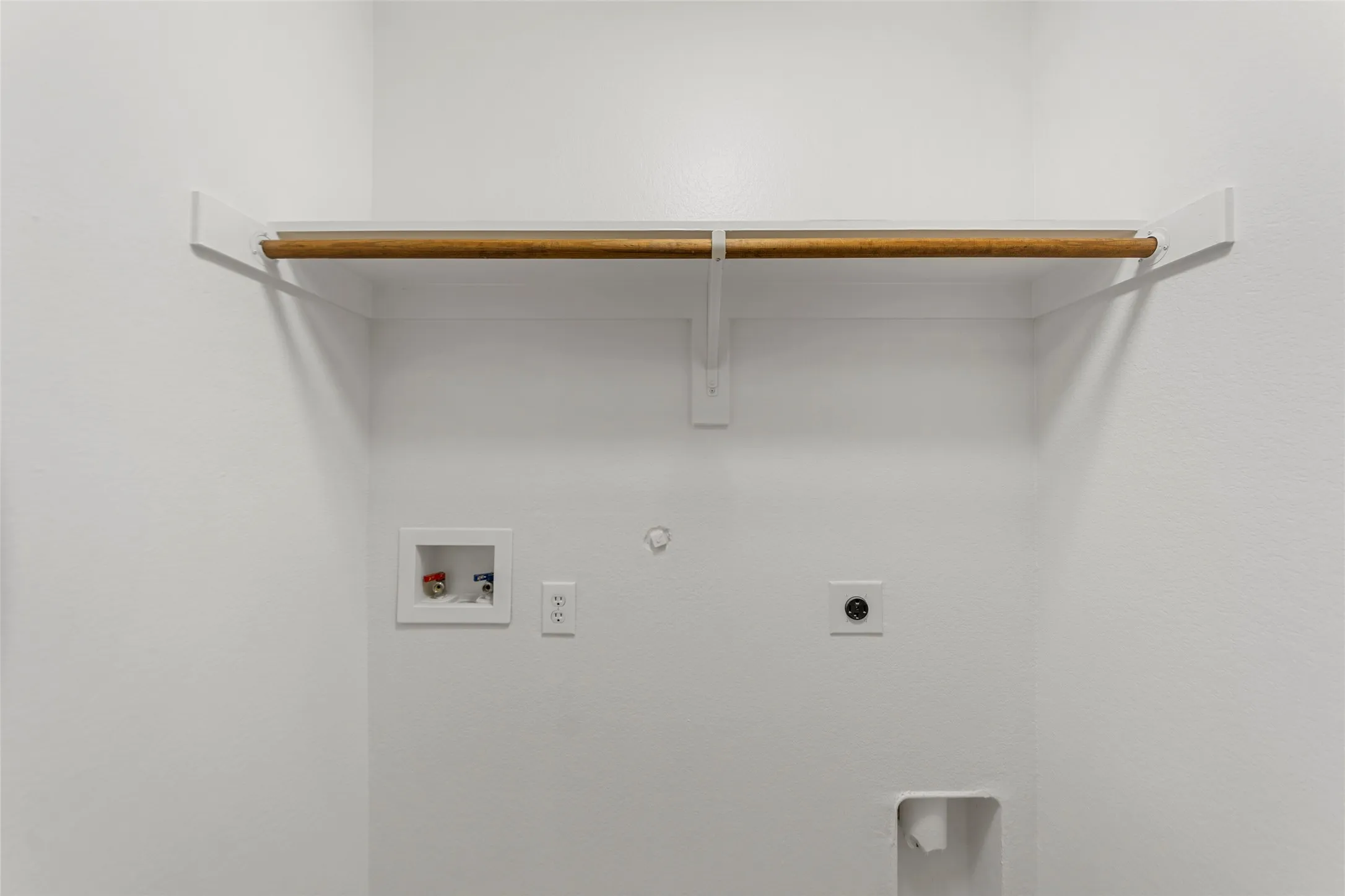 Dedicated laundry area featuring a wood-finish hanging rod, white shelving, water hookups, and electrical outlets