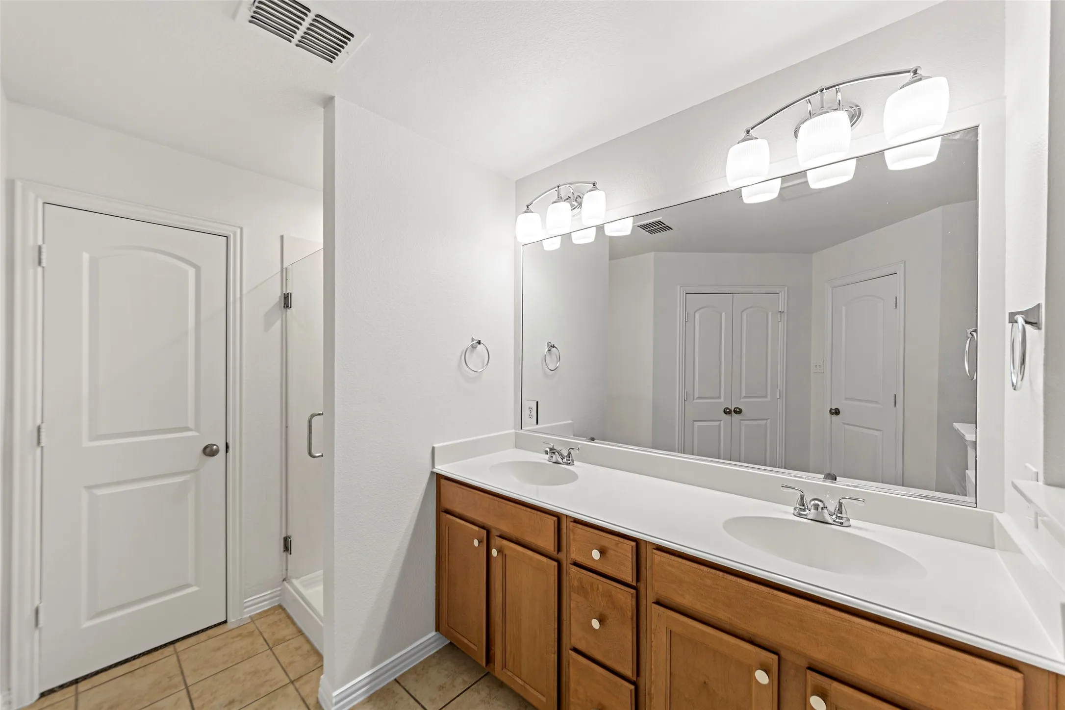 Double vanity with wood cabinetry, dual undermount sinks, and a large mirror with integrated lighting