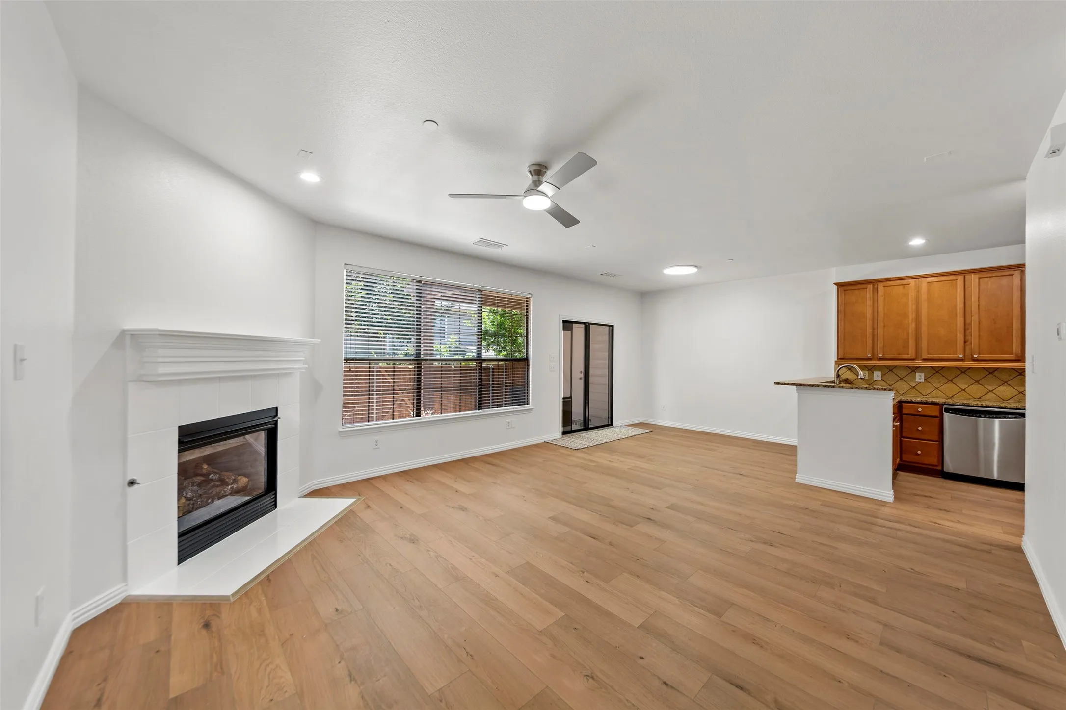 Open-concept living area featuring wood-finish flooring, a contemporary fireplace with a white mantel, and a kitchen island with seating