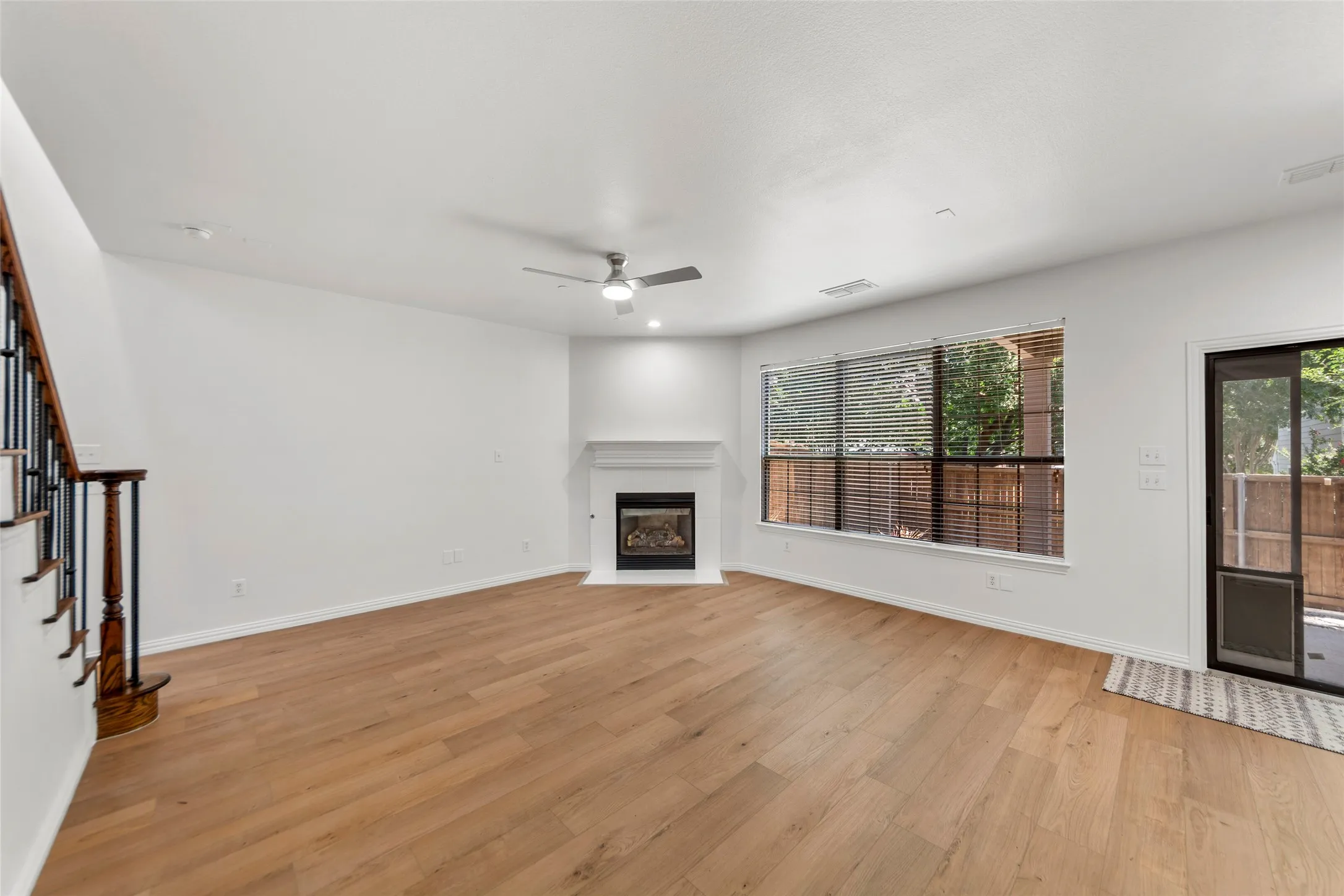 Spacious living area featuring wood-finish flooring, a corner fireplace with a white mantel, and a ceiling fan