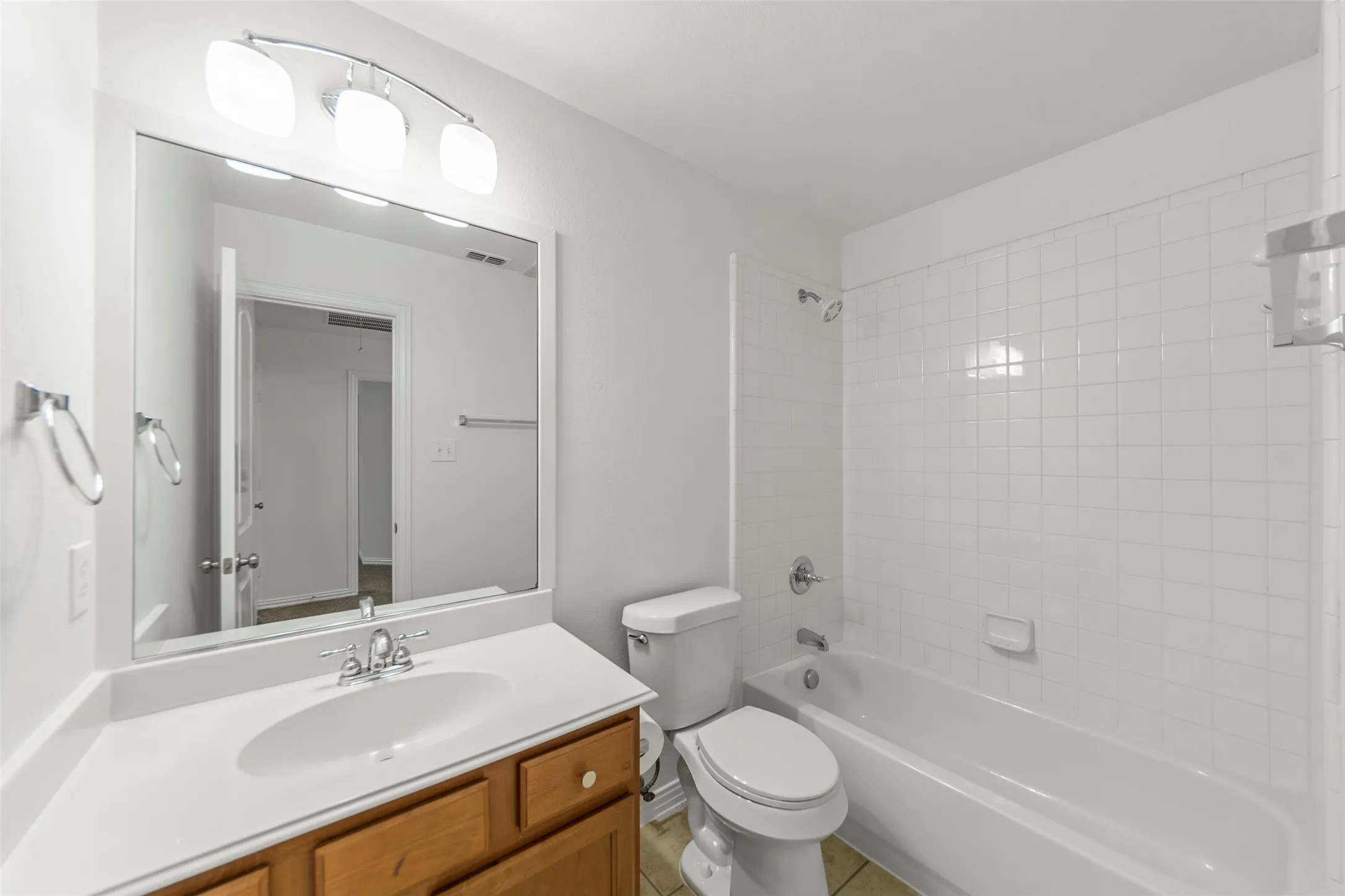 Bathroom featuring a wood-finish vanity with an integrated sink, a large wall-mounted mirror, and a three-light fixture