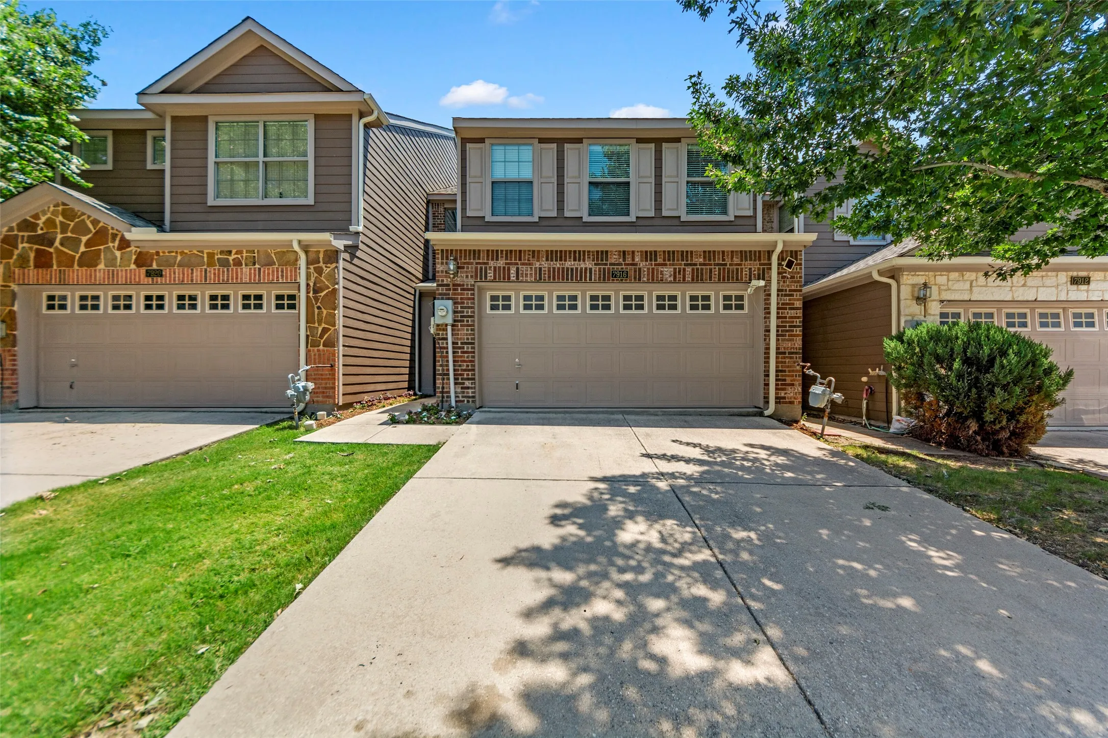Two-story residence featuring a two-car garage with paneled doors, brick veneer, and stone accents
