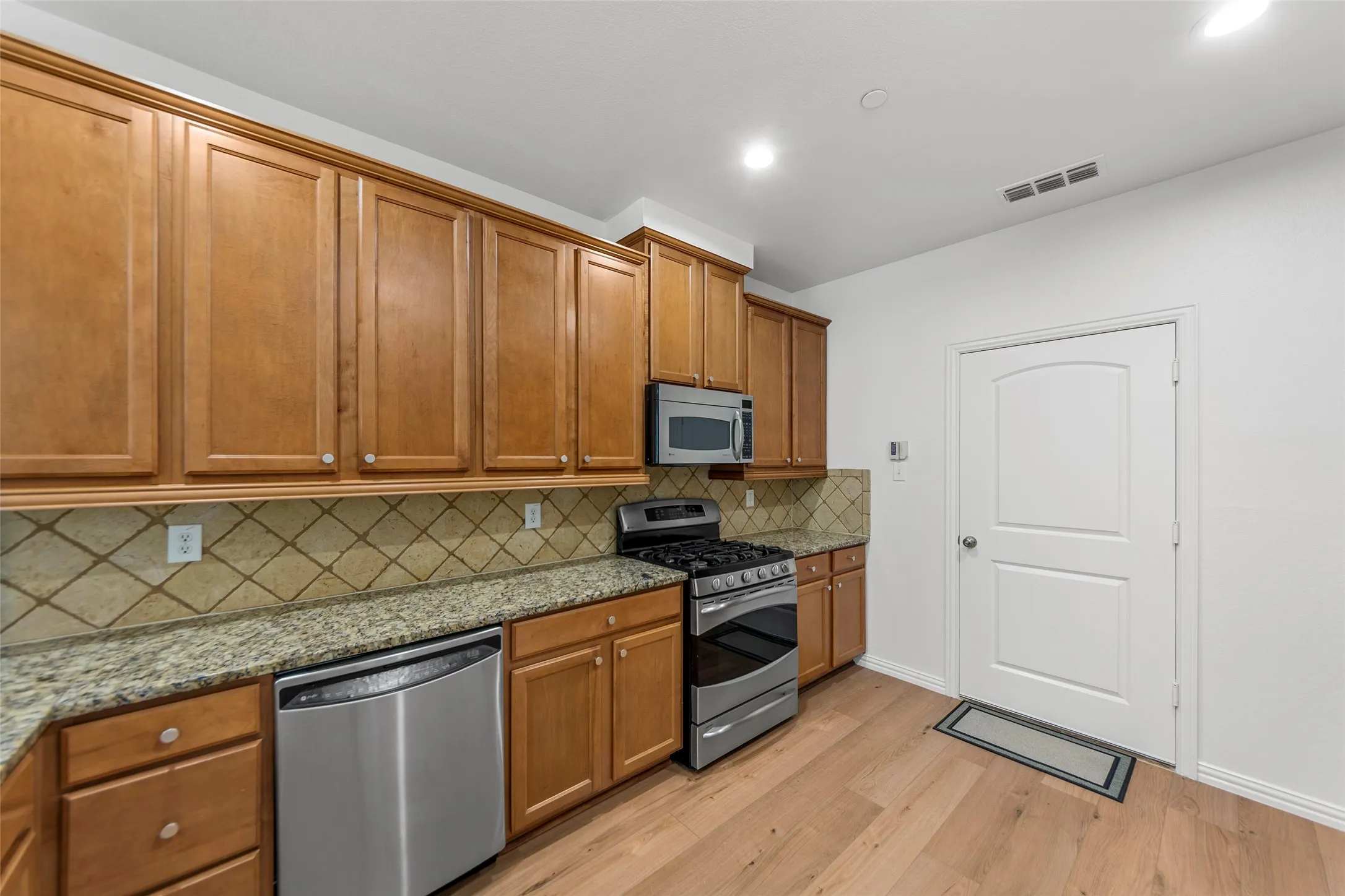 Kitchen featuring wood-finish cabinetry, stainless steel appliances, granite countertops, and a decorative tile backsplash