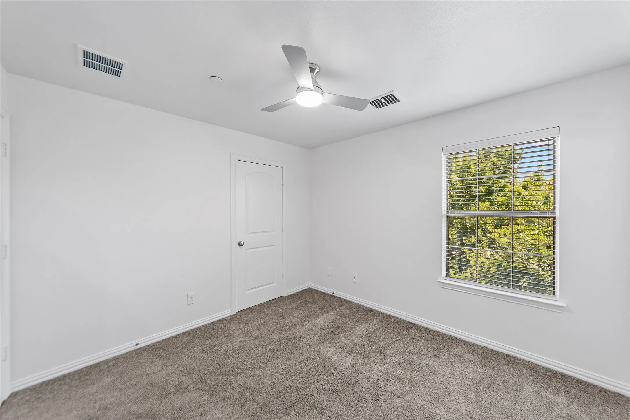 Carpeted interior room featuring a modern ceiling fan, large window with blinds, white trim, and a white interior door
