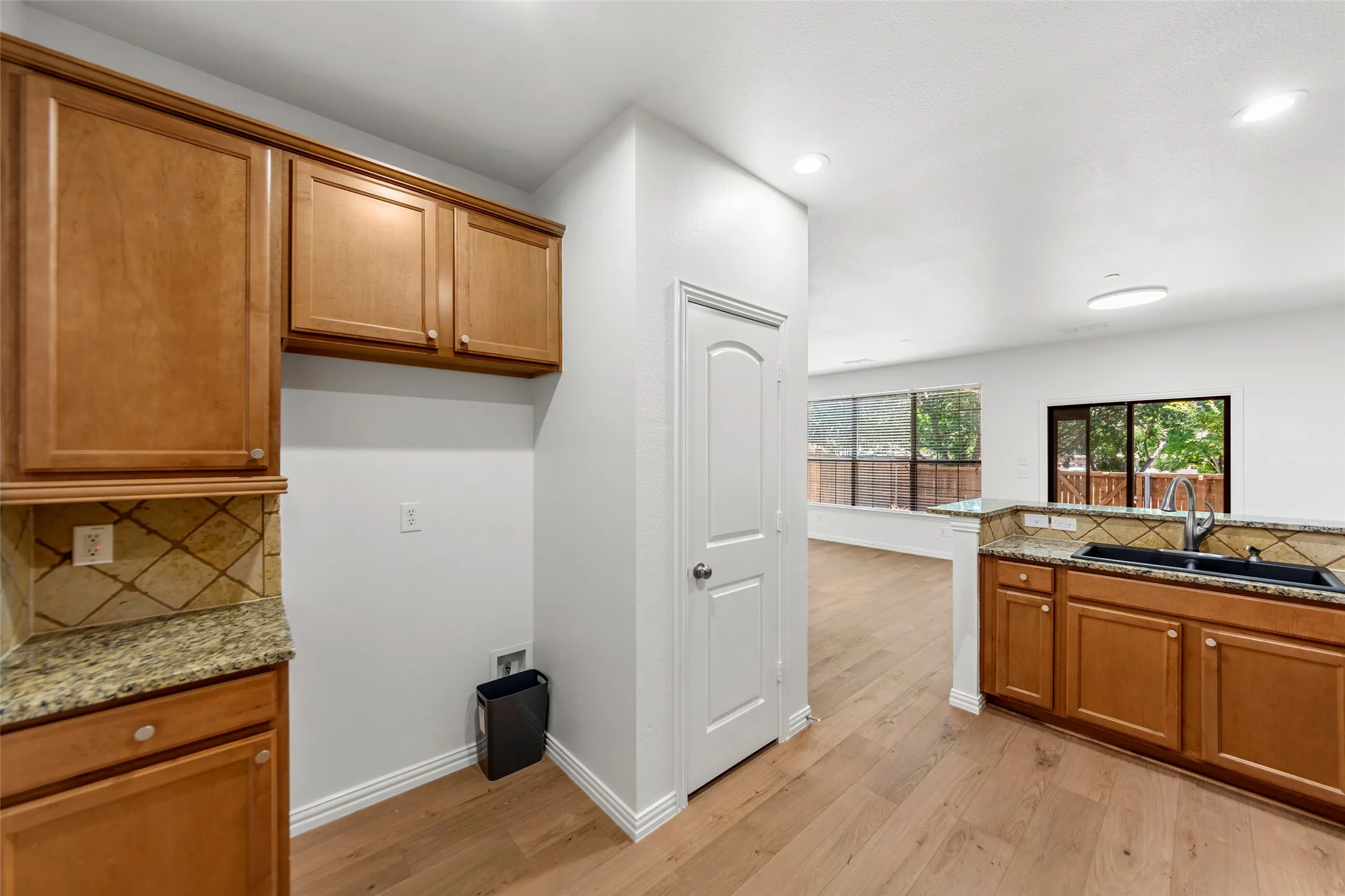 Open-concept living space featuring wood-finish flooring, recessed lighting, and a kitchen with wood cabinetry, stone countertops, and a tile backsplash