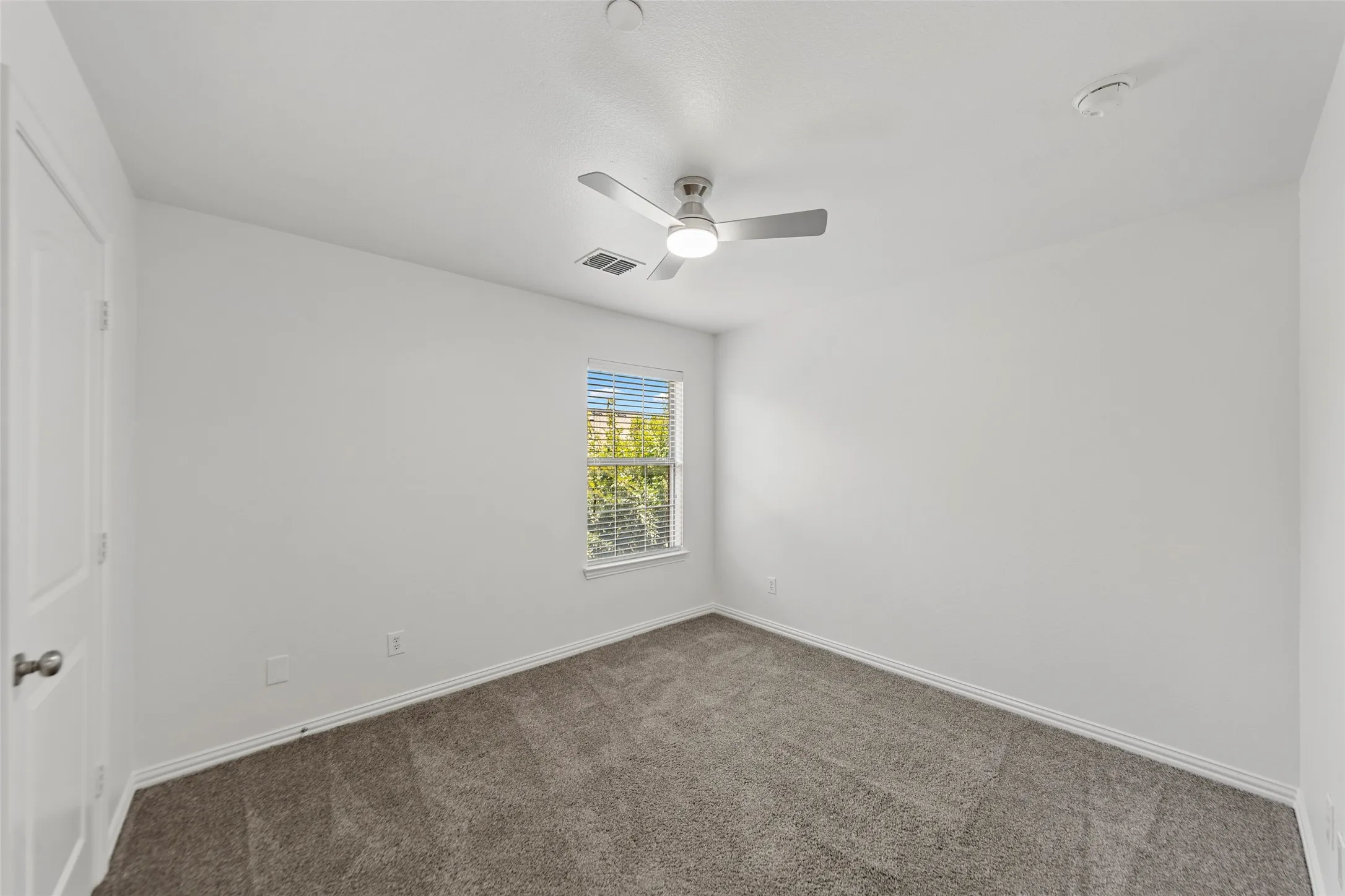 Carpeted room featuring a white door, a window with horizontal blinds, a ceiling fan with integrated lighting, and white baseboards