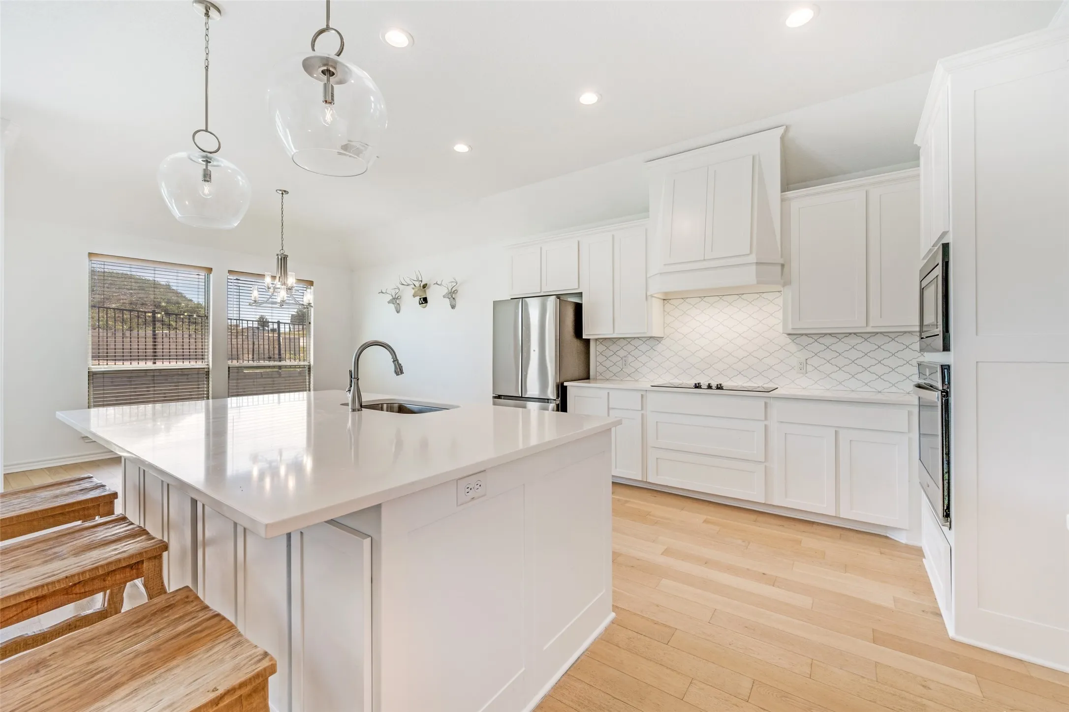 Bright kitchen featuring a substantial island with integrated sink, white cabinetry, a built-in oven, stainless steel refrigerator, and wood-finish flooring
