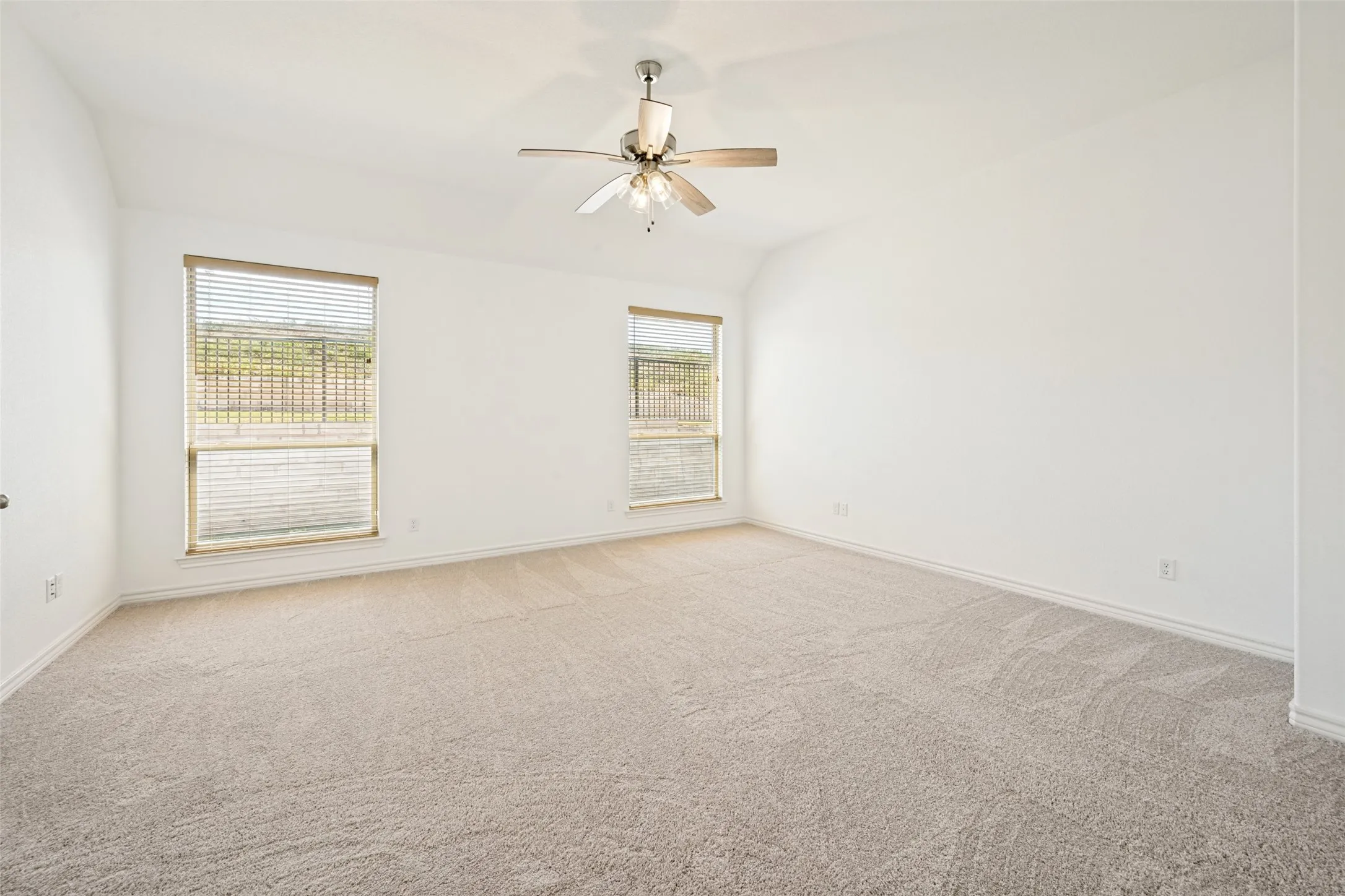 Carpeted room featuring a ceiling fan with light fixture, two windows with blinds, and white walls