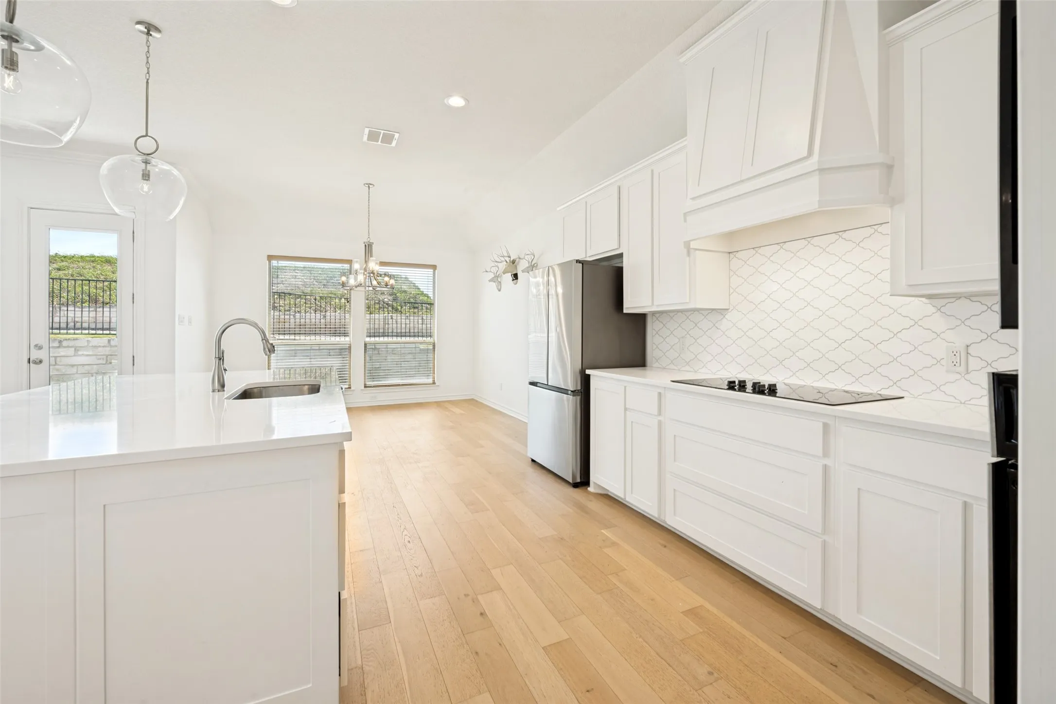 Open-concept kitchen and dining area featuring light wood-finish flooring, white cabinetry, a large kitchen island with integrated sink, and stainless steel appliances