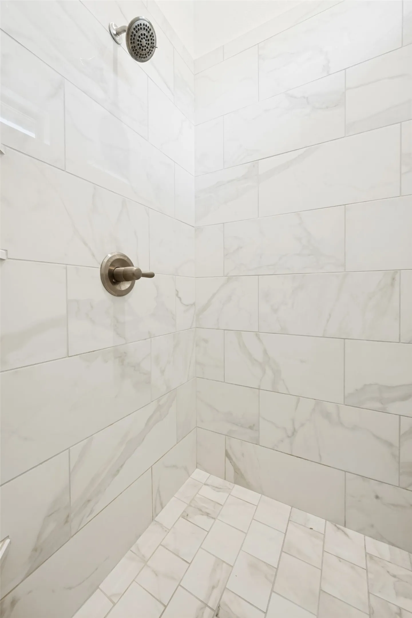 Shower featuring rectangular wall tiles with subtle veining, complementing smaller rectangular floor tiles