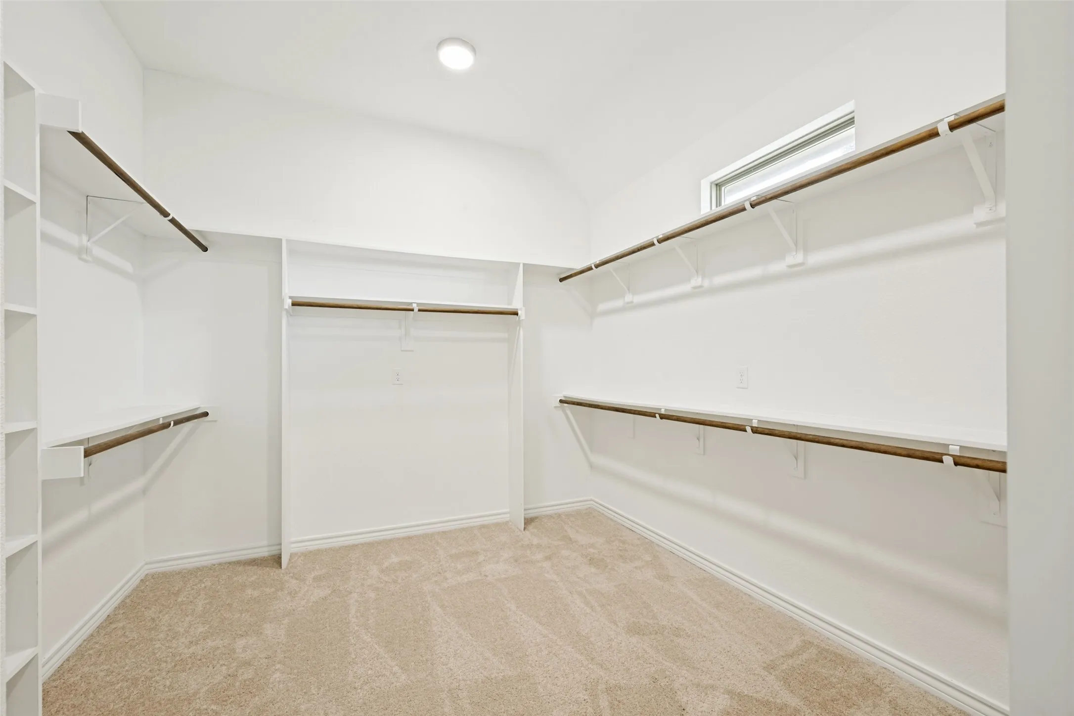 Spacious walk-in closet featuring white built-in shelving, wood-finish hanging rods, neutral carpet flooring, and a recessed ceiling light