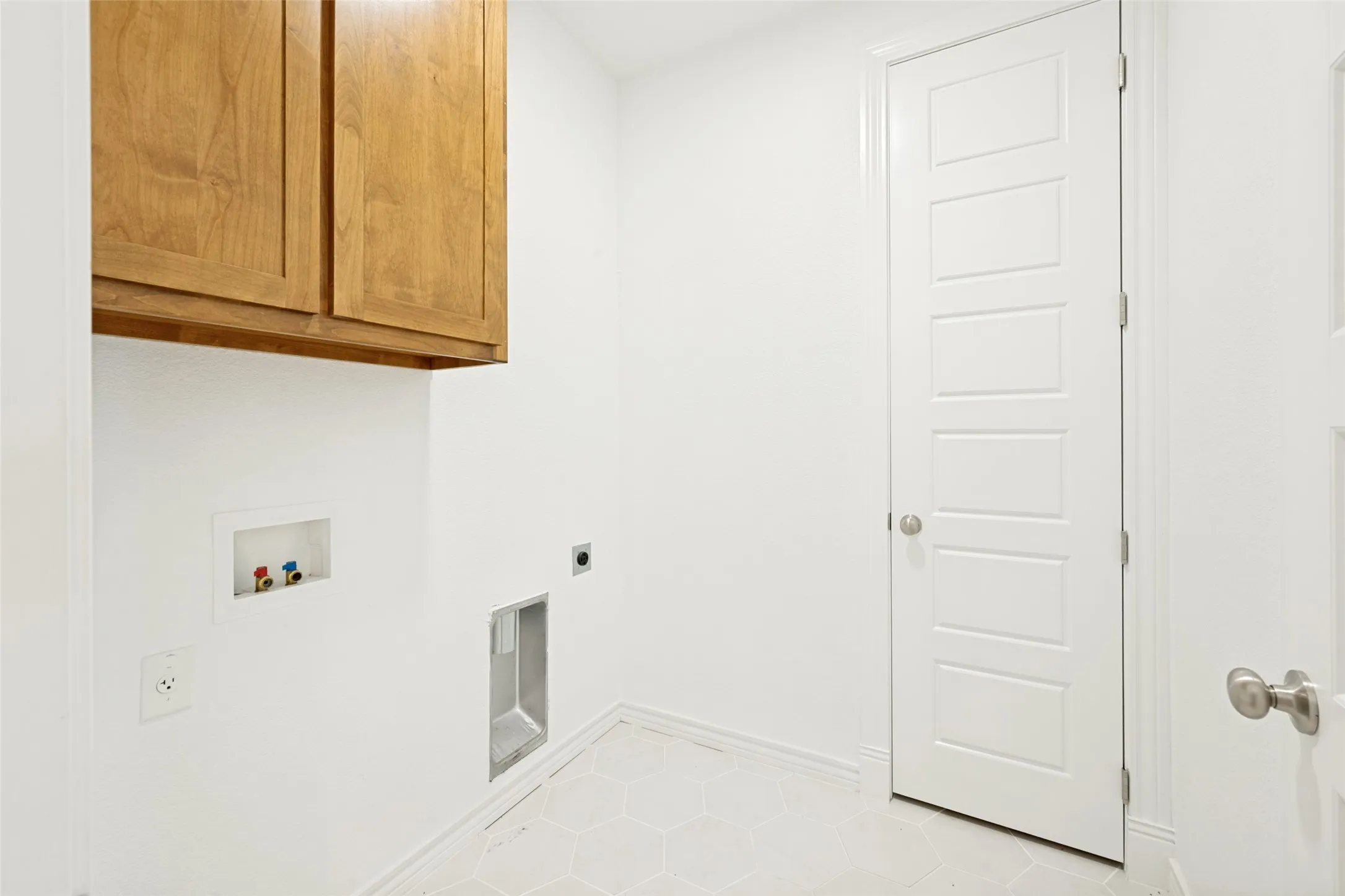 Utility room featuring wood cabinetry, white walls, and a patterned tile floor