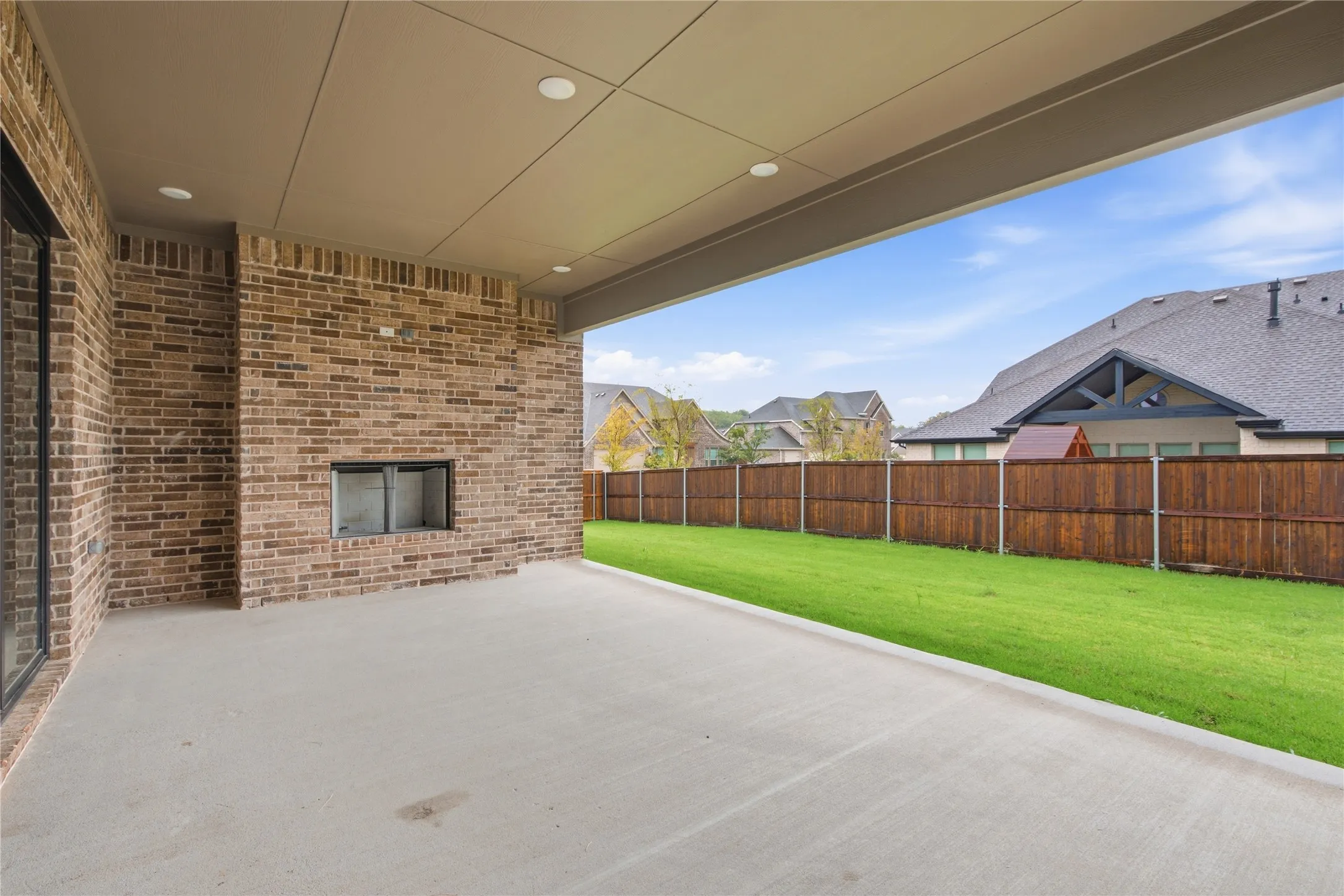 Covered patio featuring a brick-clad outdoor fireplace, concrete flooring, and recessed lighting
