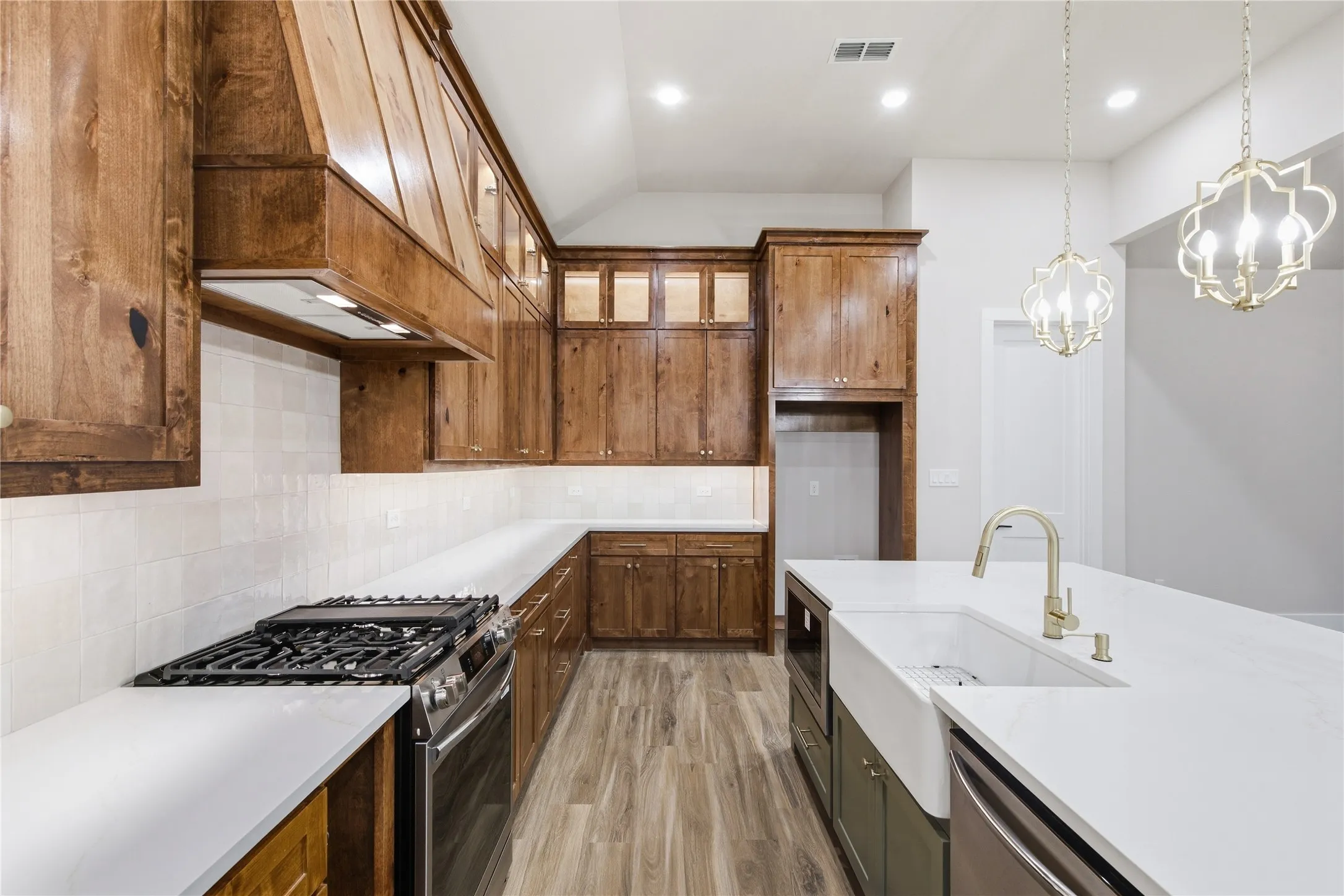 Spacious kitchen featuring extensive wood cabinetry, white countertops, a large farmhouse sink, stainless steel appliances, and decorative pendant lighting
