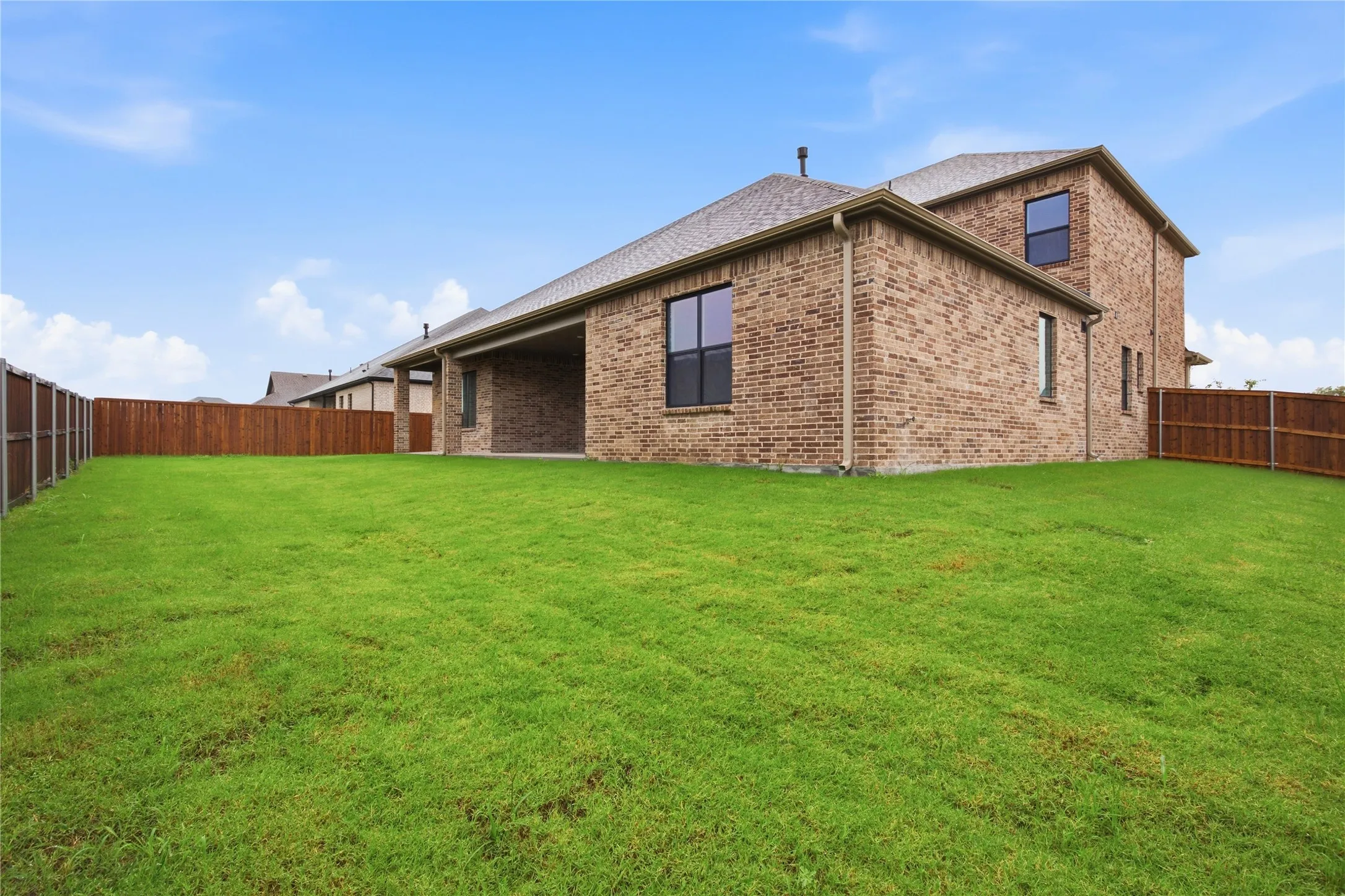 Expansive green lawn with a two-story brick exterior and a covered patio