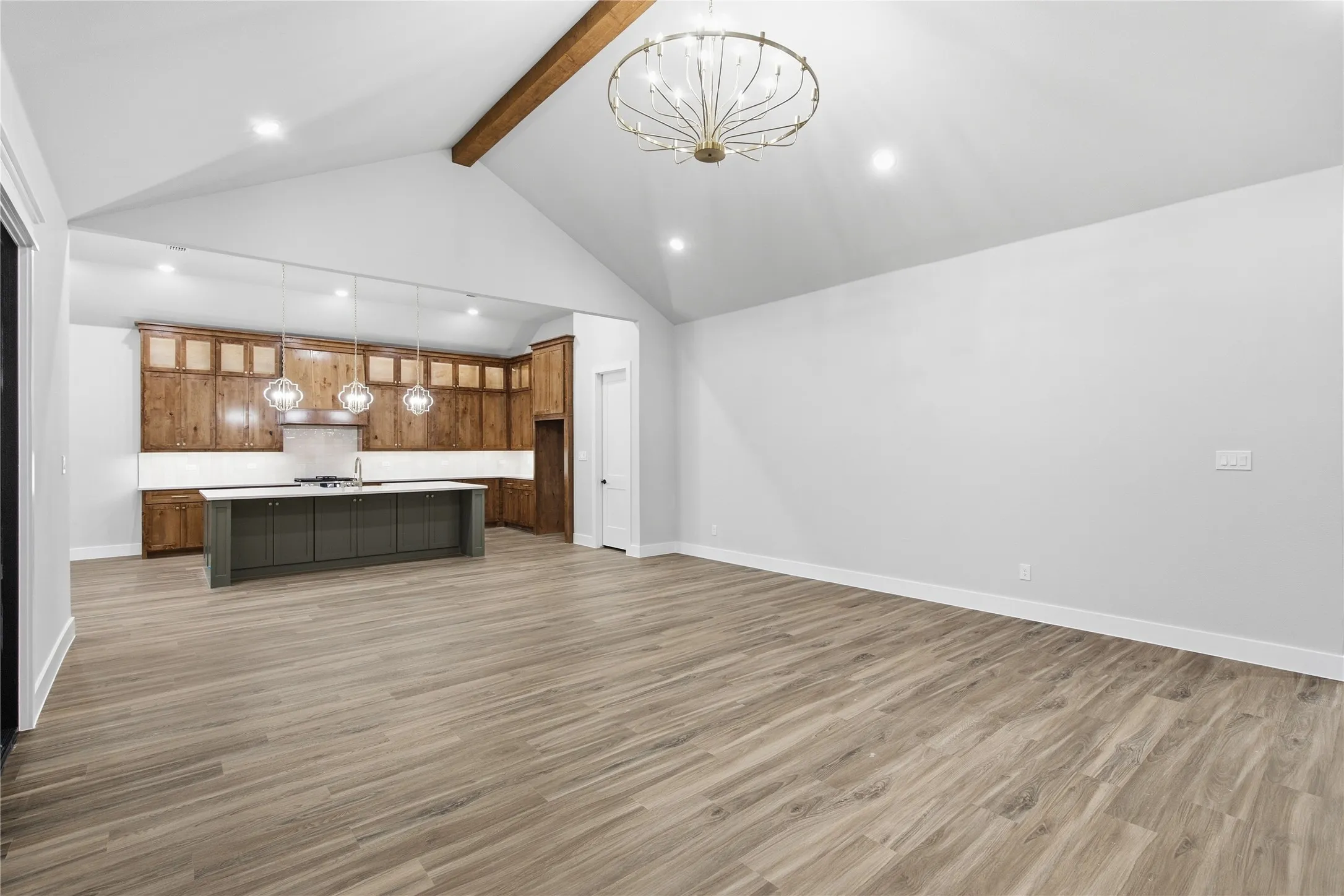 Vaulted ceiling with exposed wood beam, wood-finish flooring, recessed lighting, kitchen with wood cabinetry and contrasting island, pendant lighting over island