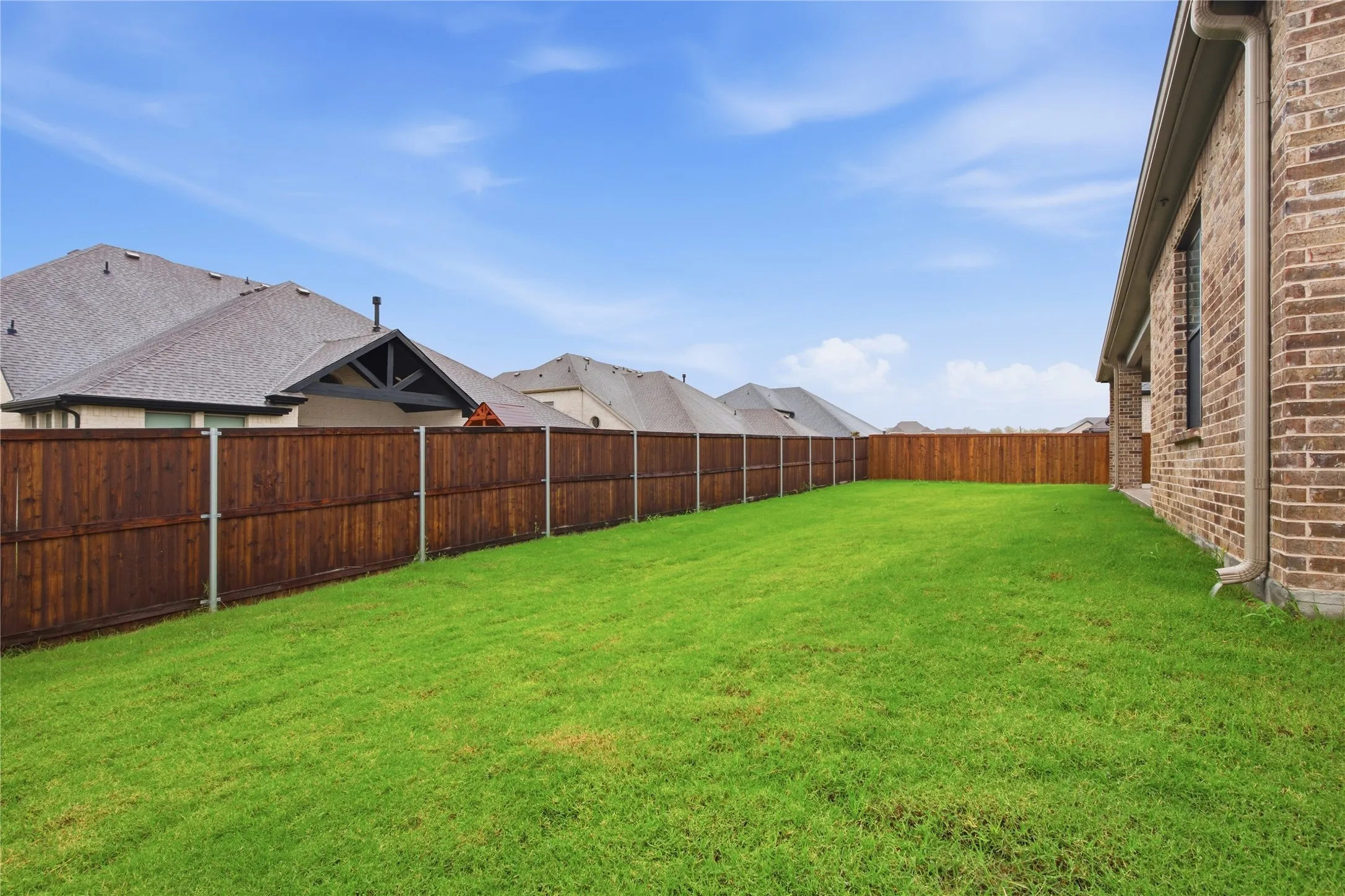 Expansive green lawn with a durable wood privacy fence and a brick exterior
