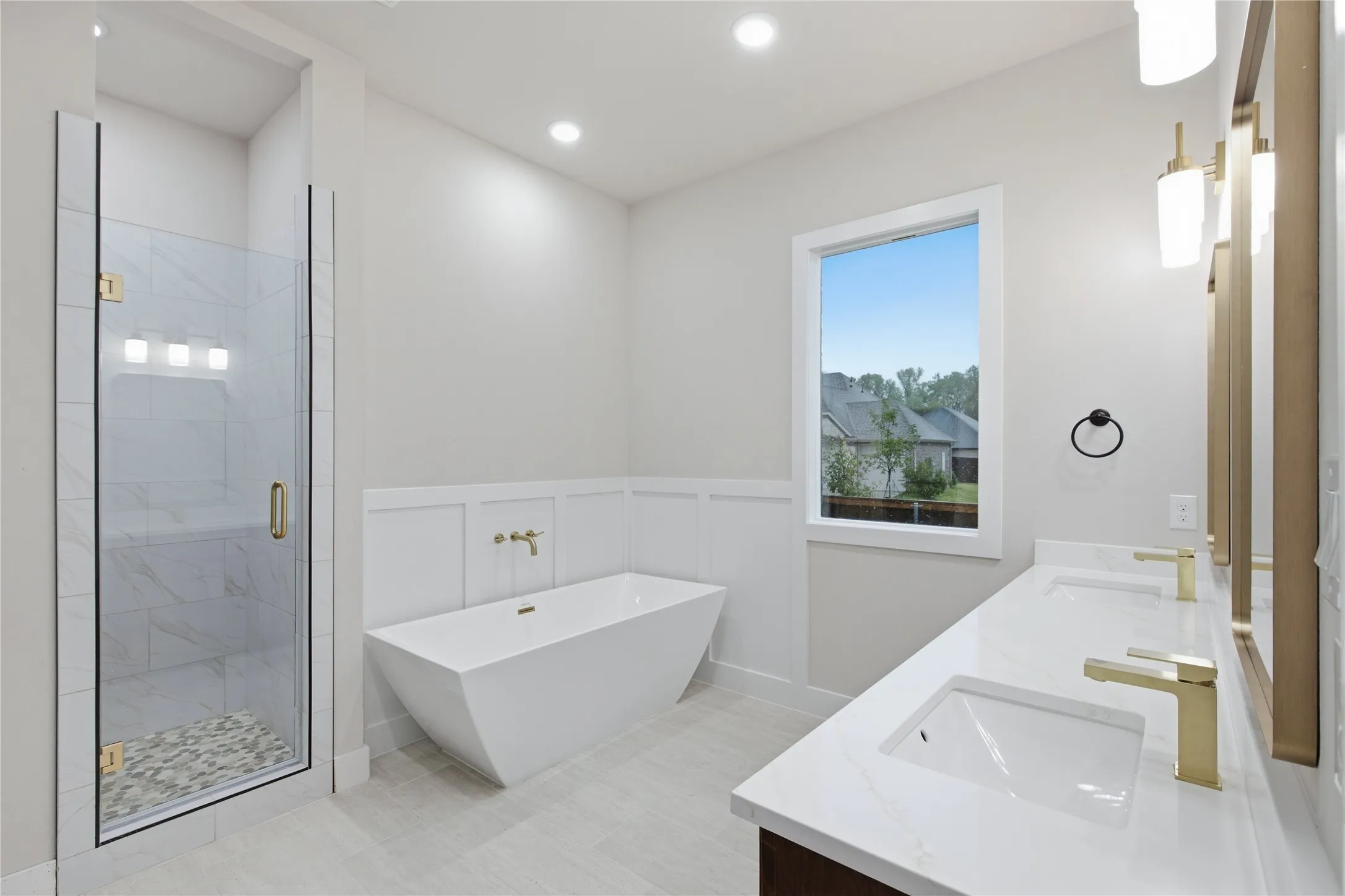 Walk-in shower with glass enclosure, freestanding soaking tub, dual vanity with undermount sinks, and gold-finish fixtures