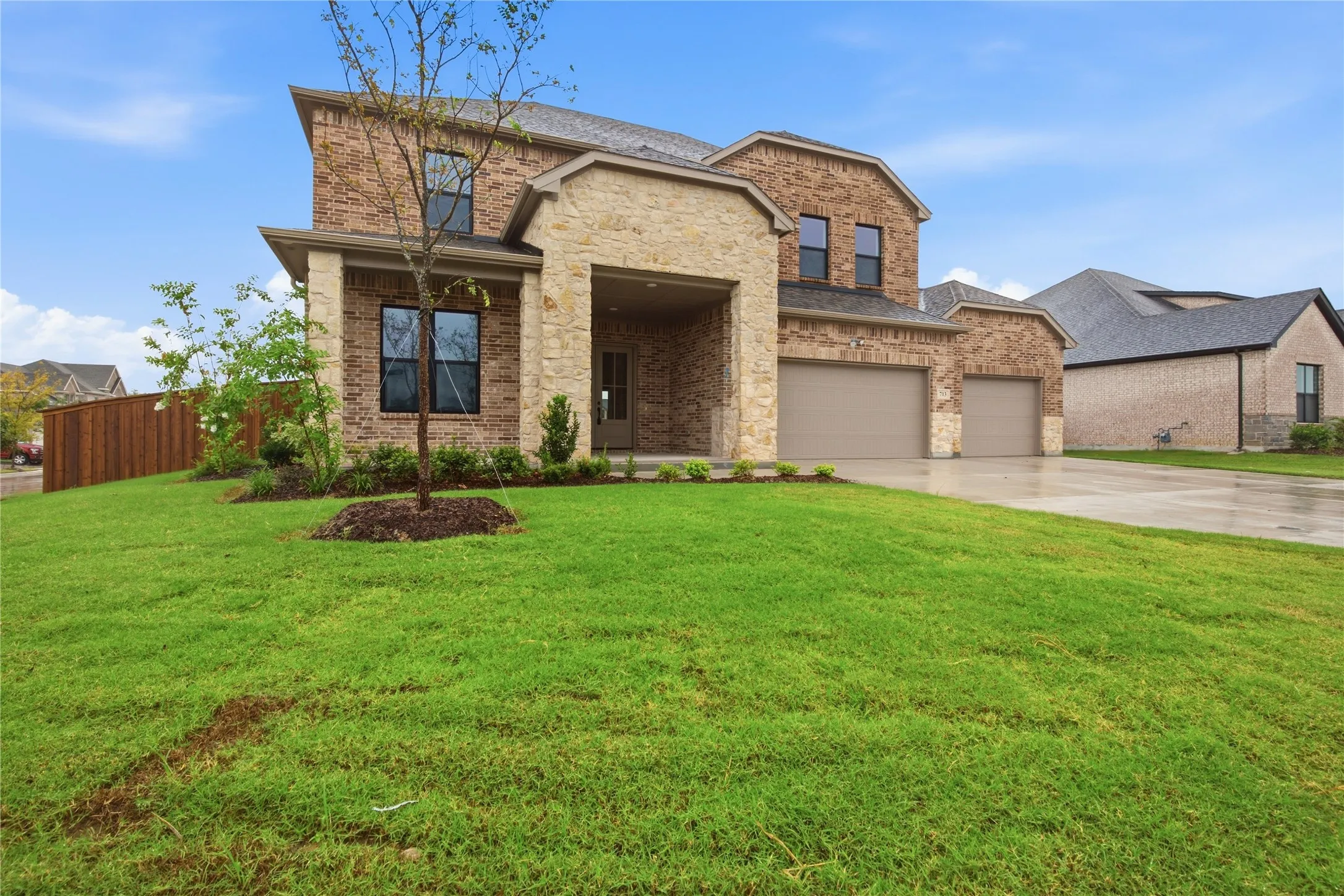Brick and stone exterior, covered entry, multiple windows with dark frames, two-car garage, landscaped front yard