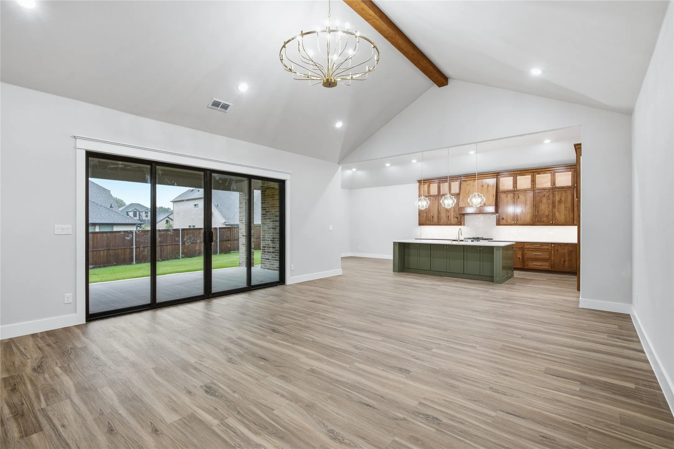 Vaulted ceiling with an exposed wood beam, contemporary chandelier, wood-finish flooring, multi-panel sliding glass door, and a kitchen featuring a green island with pendant lighting