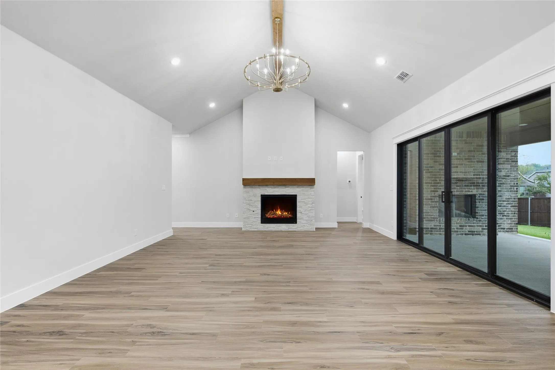 Vaulted ceiling with an ornate chandelier, wood-finish flooring, a fireplace featuring a wood mantel and stone surround, and multi-panel sliding glass doors