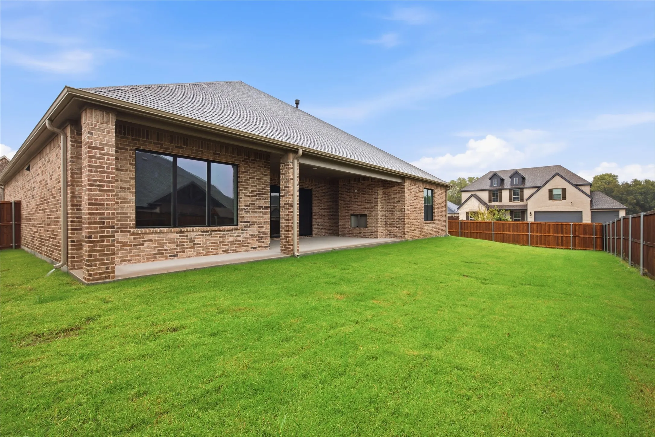 Brick exterior with covered patio, expansive lawn, and privacy fencing