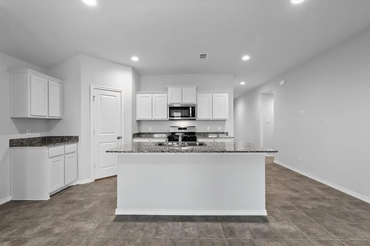 Kitchen featuring an island with a double basin sink, white cabinetry, granite countertops, built-in microwave, and tile flooring