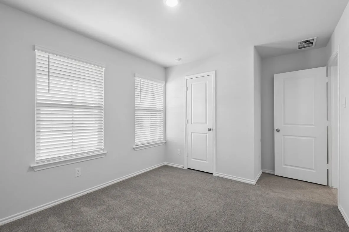 Carpeted room featuring two windows with blinds, white trim, and two paneled doors