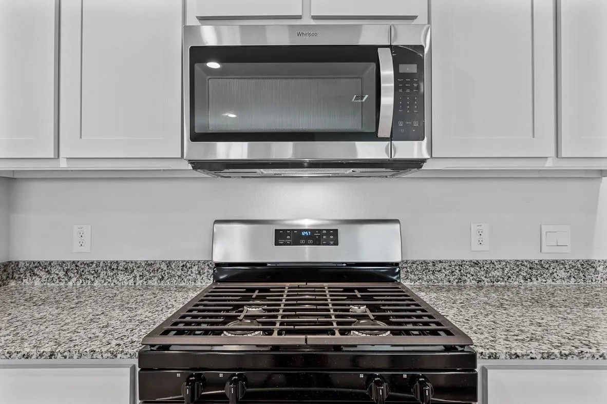 Kitchen featuring a stainless steel microwave, gas range, shaker-style cabinetry, and speckled countertops