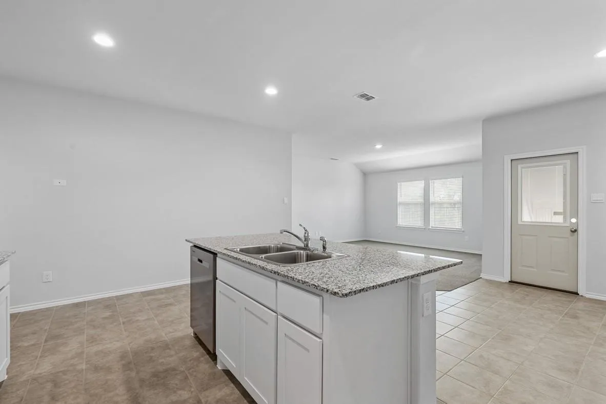 Kitchen island featuring a dual basin sink, stainless steel dishwasher, and a light-toned countertop