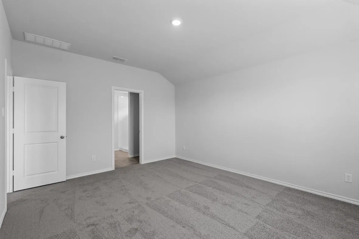 Spacious carpeted room featuring a white paneled door, light gray walls, a sloped ceiling, and recessed lighting
