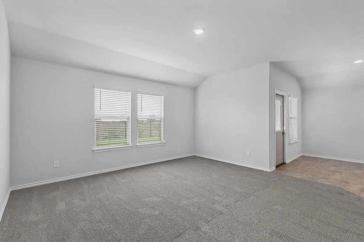 Spacious room featuring neutral grey carpeting, light grey walls, and two windows with blinds