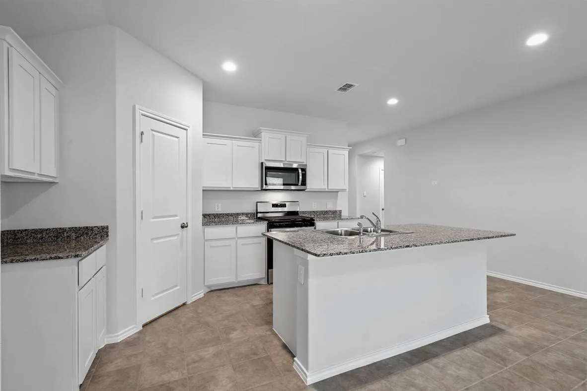 Kitchen featuring a central island with an undermount double-bowl sink, white cabinetry, integrated stainless steel appliances, speckled stone countertops, and tile flooring