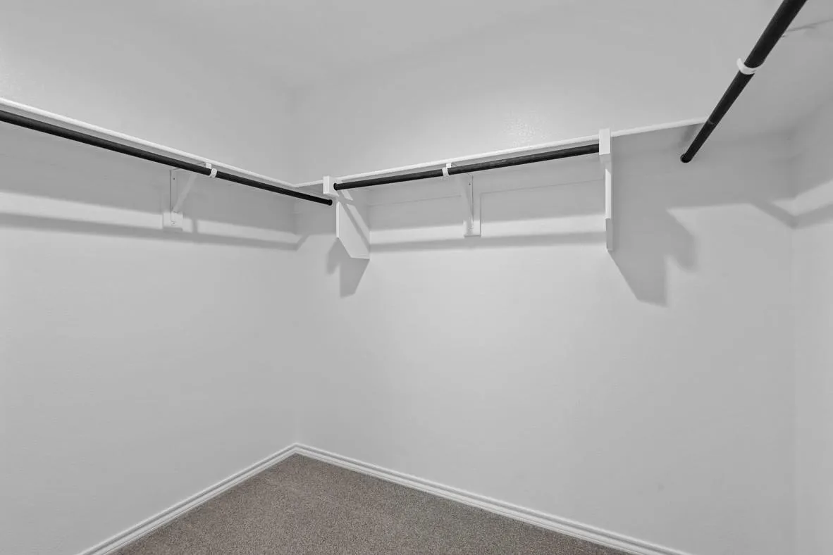 Walk-in closet featuring white shelving and black hanging rods