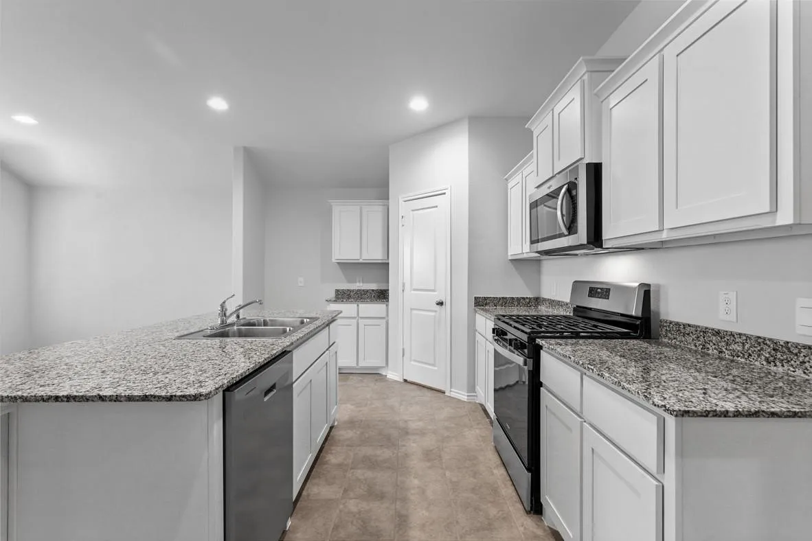 Kitchen featuring stainless steel appliances, white cabinetry, a double basin sink, and ample countertop space