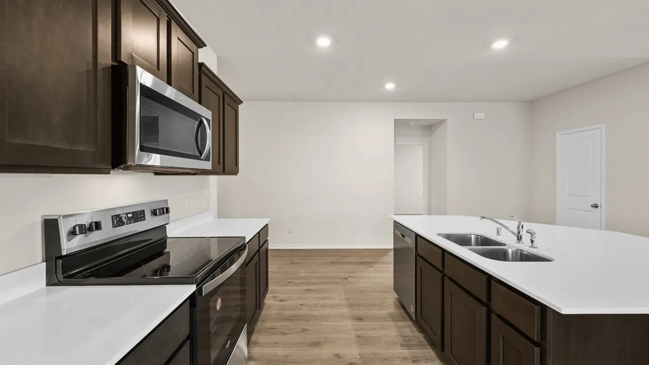 Kitchen featuring wood-finish flooring, dark wood cabinetry, white countertops, stainless steel appliances, and an island with a dual-basin sink