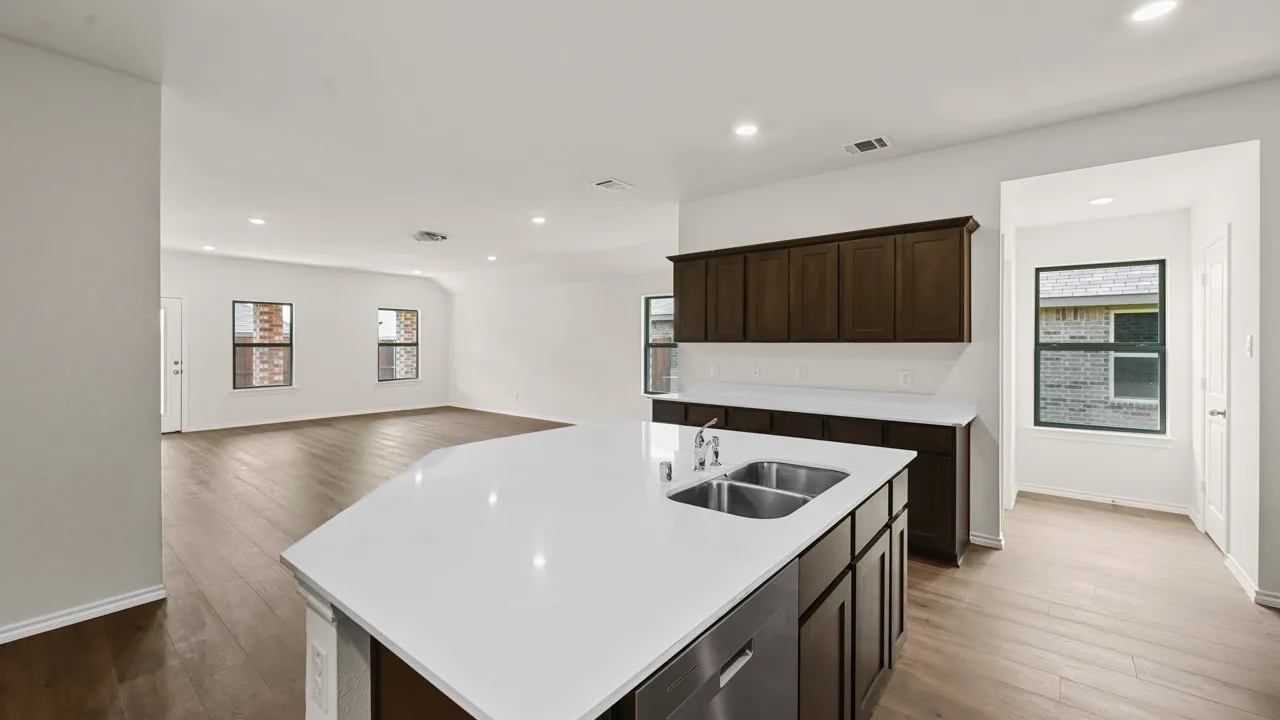 Kitchen island with white countertop and integrated double basin sink, dark wood-finish cabinetry, and wood-finish flooring extending into the living area