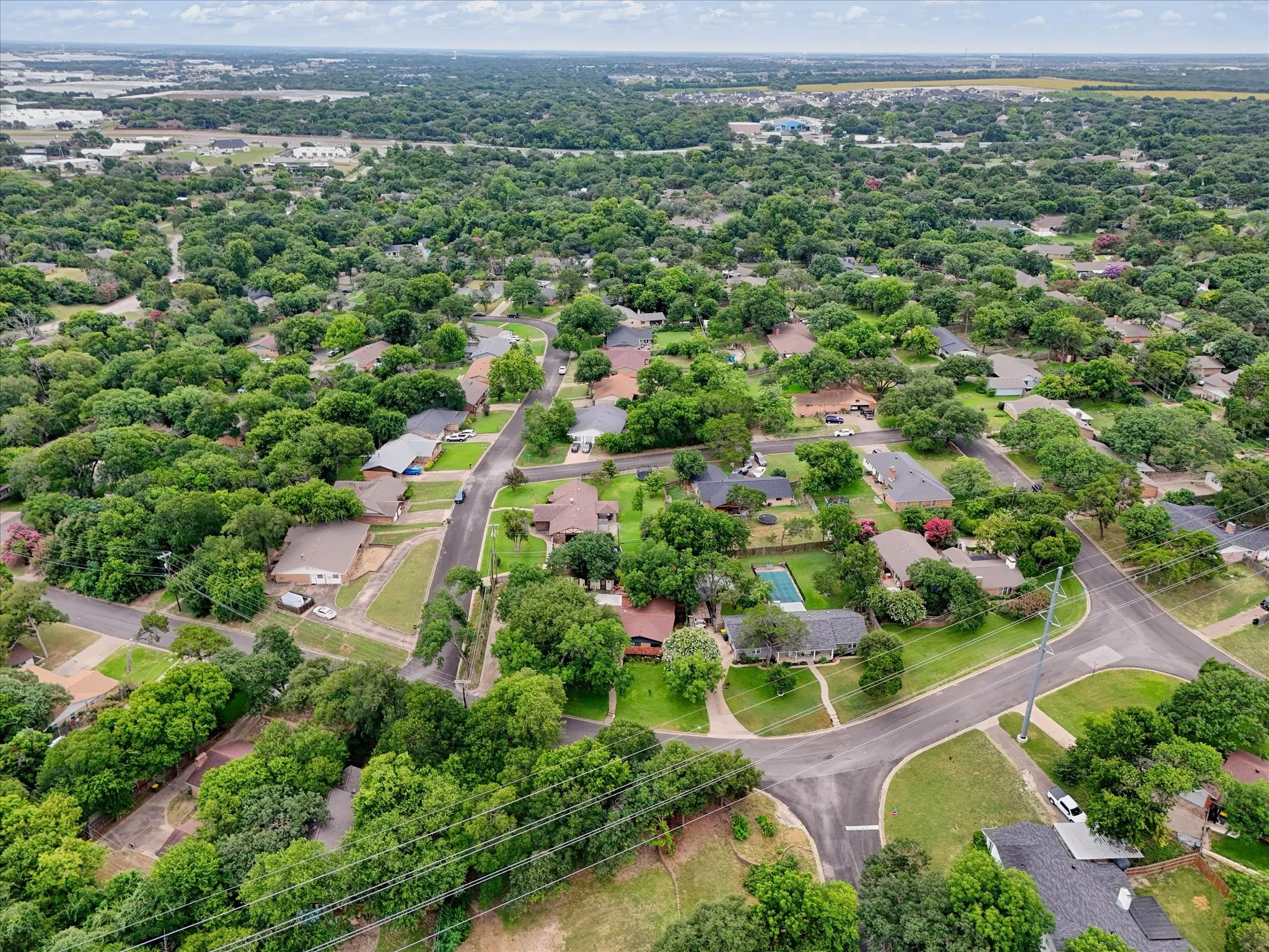 Expansive aerial perspective showcasing a residential neighborhood with abundant mature tree cover and curving street layouts