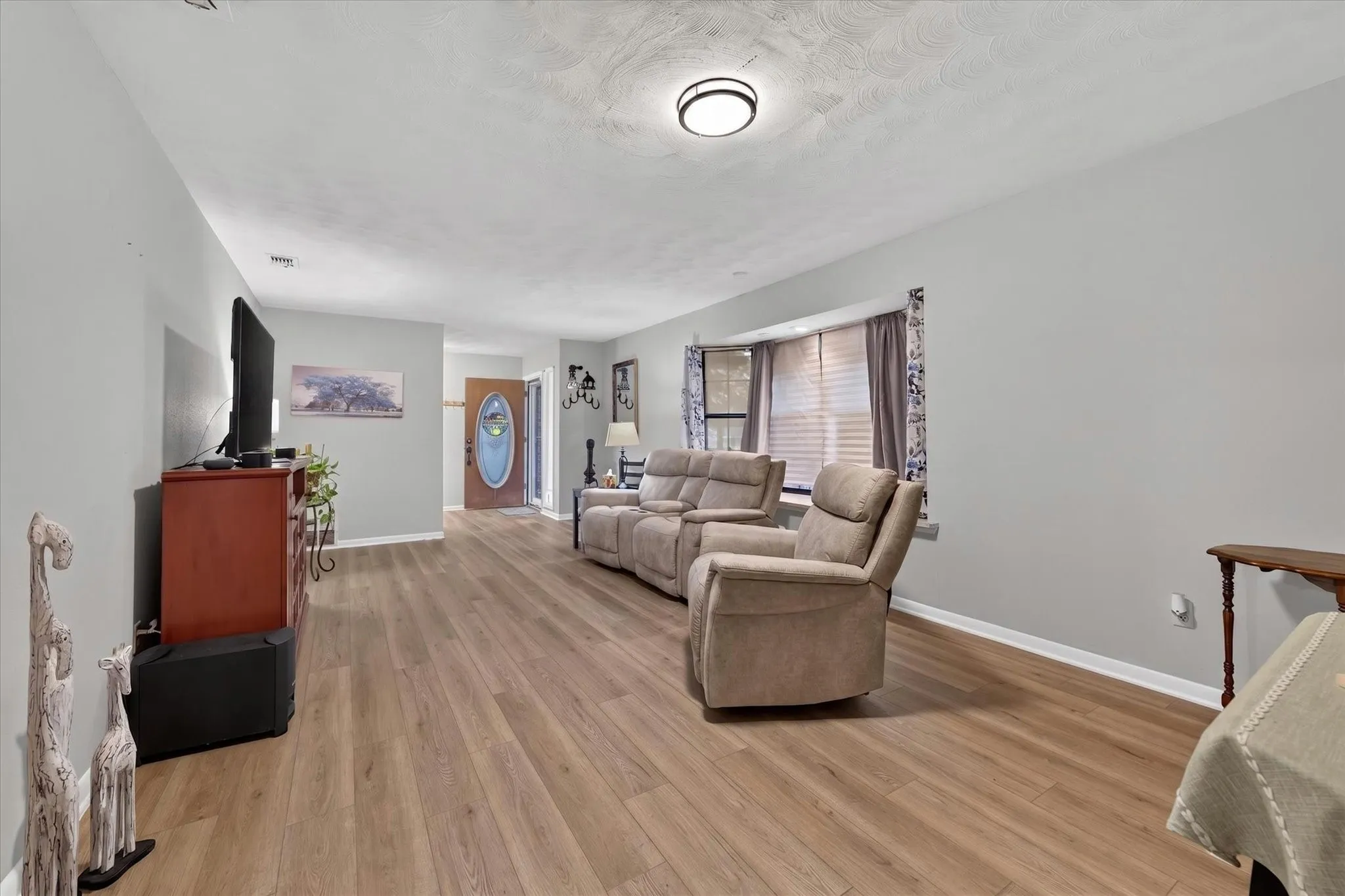 Spacious living area featuring wood-finish flooring, light gray walls, and a recessed bay window with blinds