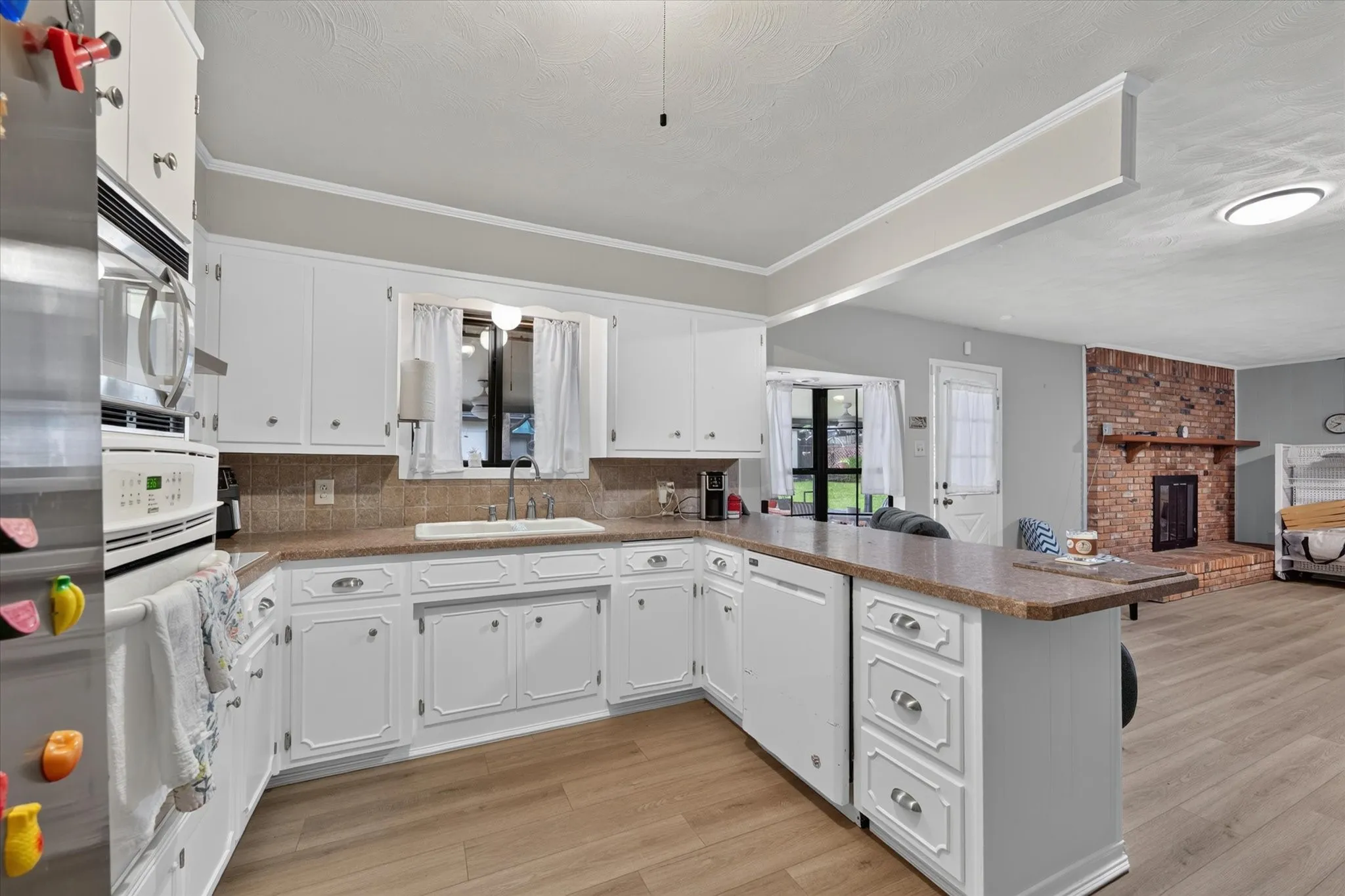 Kitchen featuring white cabinetry, integrated wall oven, built-in dishwasher, and a peninsula with countertop seating
