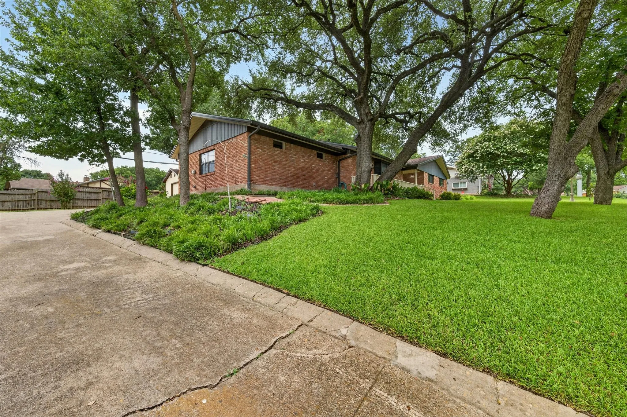 Brick exterior with a gabled roofline, mature trees, landscaped shrubbery, and an expansive lawn area