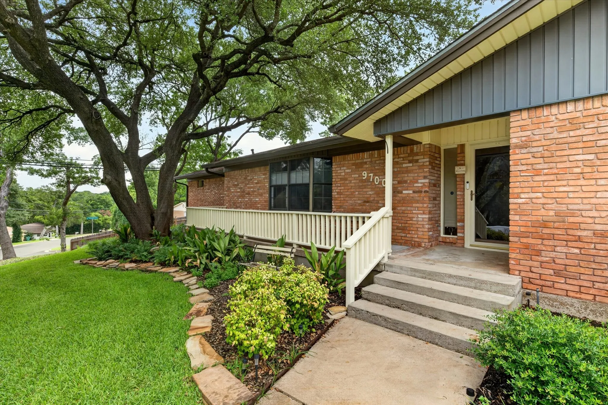Brick exterior with dark gray vertical siding accents, concrete walkway, and stone-edged landscaping