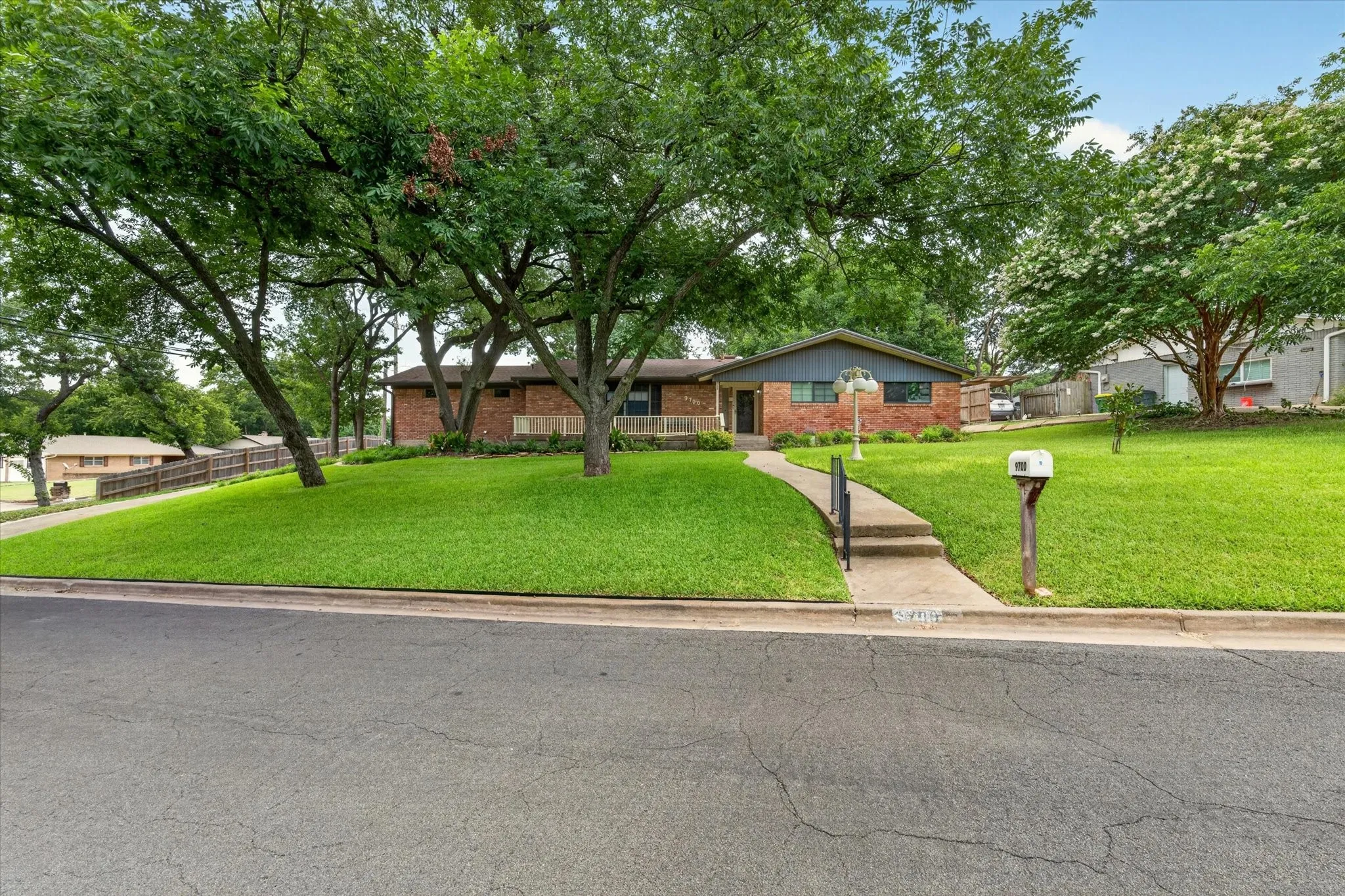 Brick and siding home featuring a front lawn with mature trees and a concrete walkway