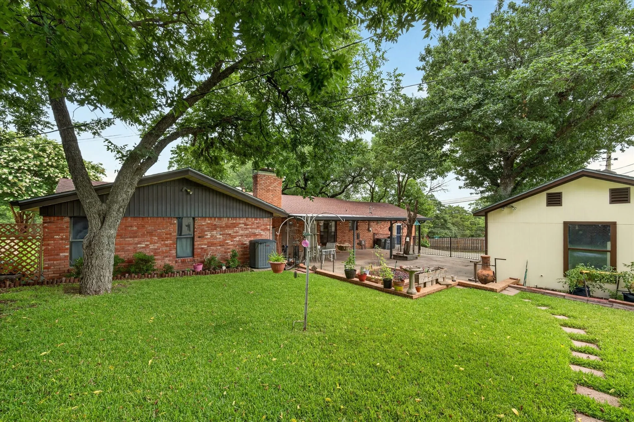 Spacious backyard featuring a lush lawn, mature trees, brick patio, and a separate structure with a light-colored exterior