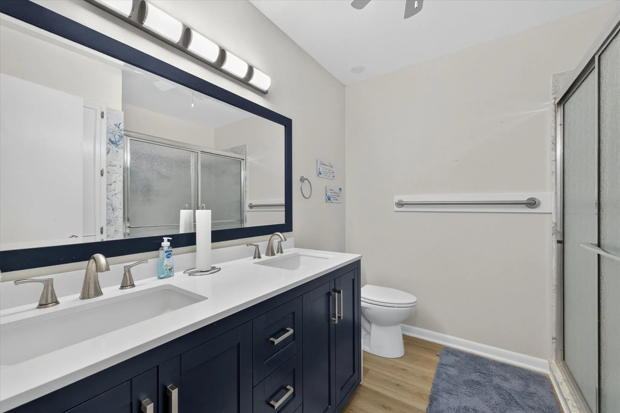 Dual-sink vanity with a white countertop and navy cabinetry, brushed nickel hardware, a framed mirror, and a glass-enclosed shower