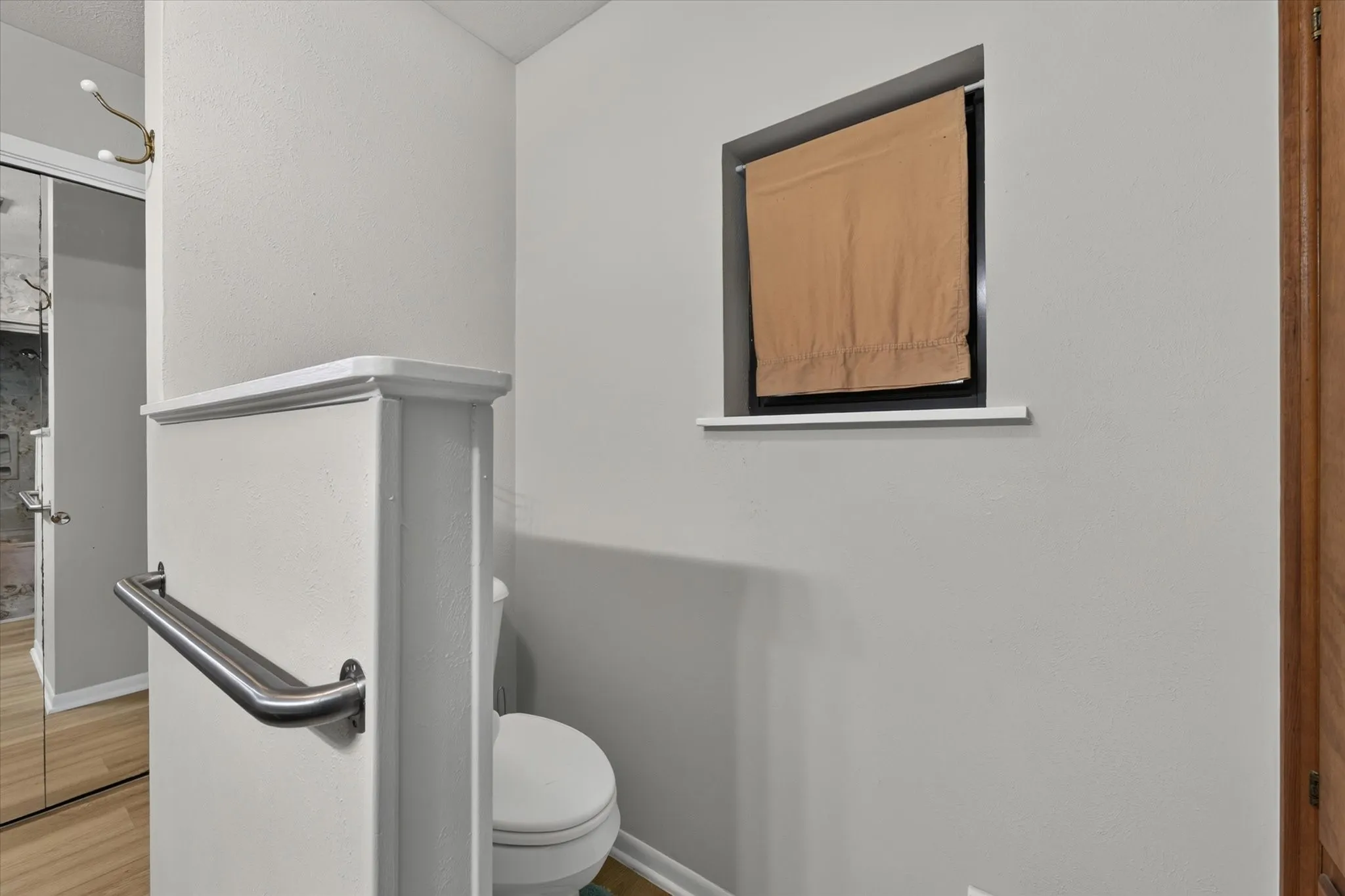 Compact water closet featuring a white toilet, light gray painted walls, and a built-in window with a ledge