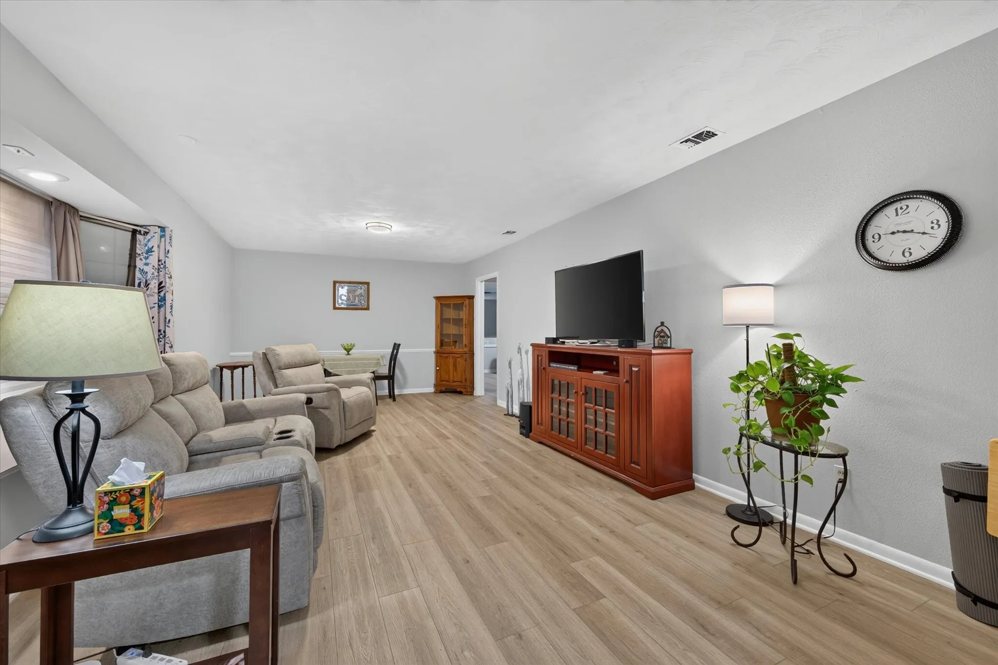 Spacious room with wood-finish flooring, light grey wall paint, recessed lighting, and white baseboards