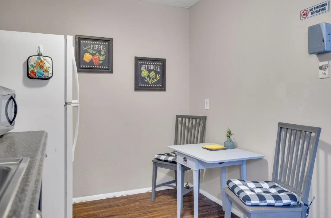 Compact kitchen area with wood-finish flooring, a white refrigerator, a built-in stainless steel sink, and a countertop with a dark finish