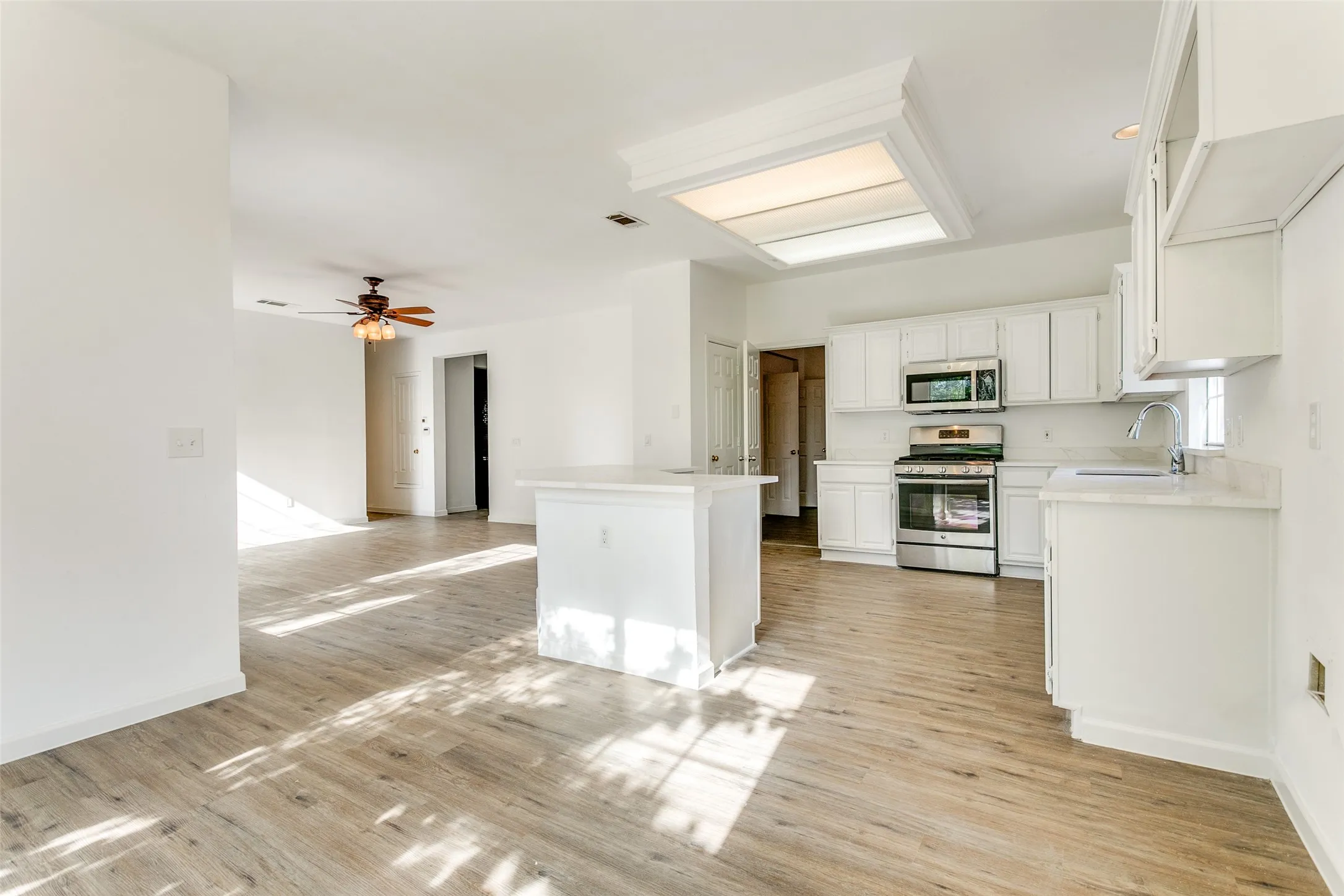 Kitchen featuring stainless steel appliances, white cabinets, sink, light wood-type flooring, and ceiling fan